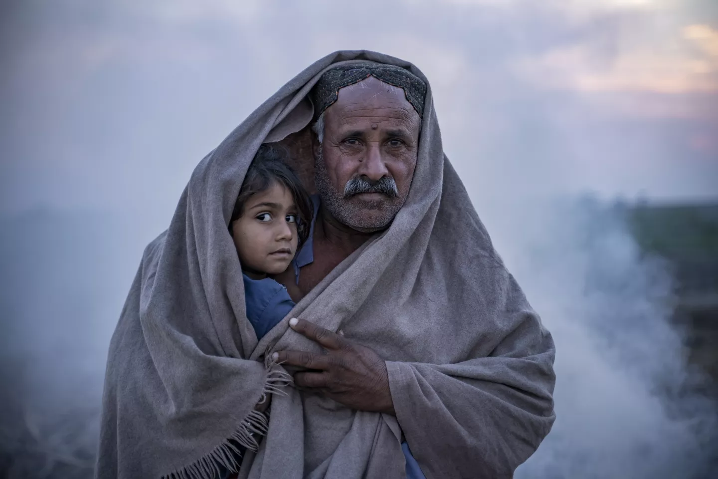 Pakistan. A man wrapped in a blanket carries his daughter in Dadu District, Sindh Province, Pakistan.