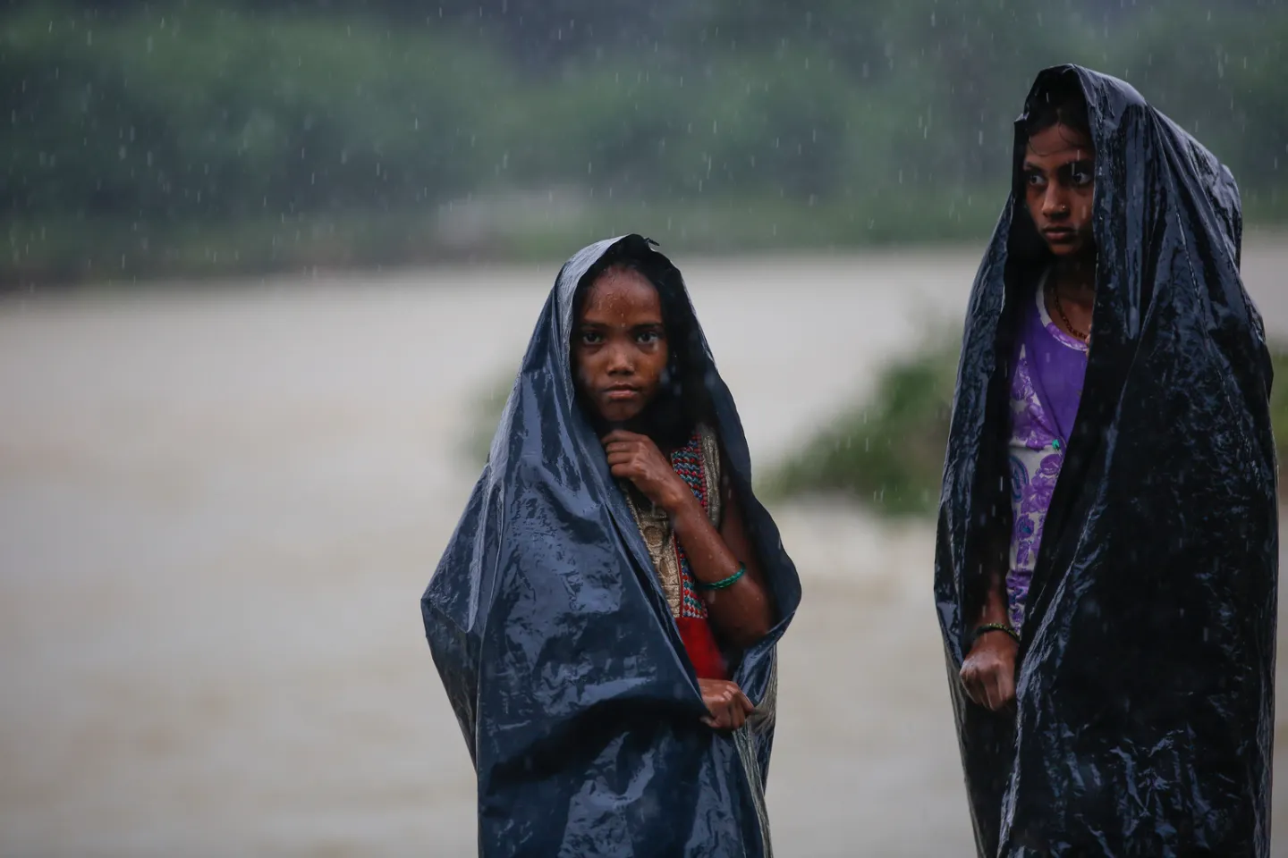 Two girls use plastic sheets to hide from the rain in Nepal