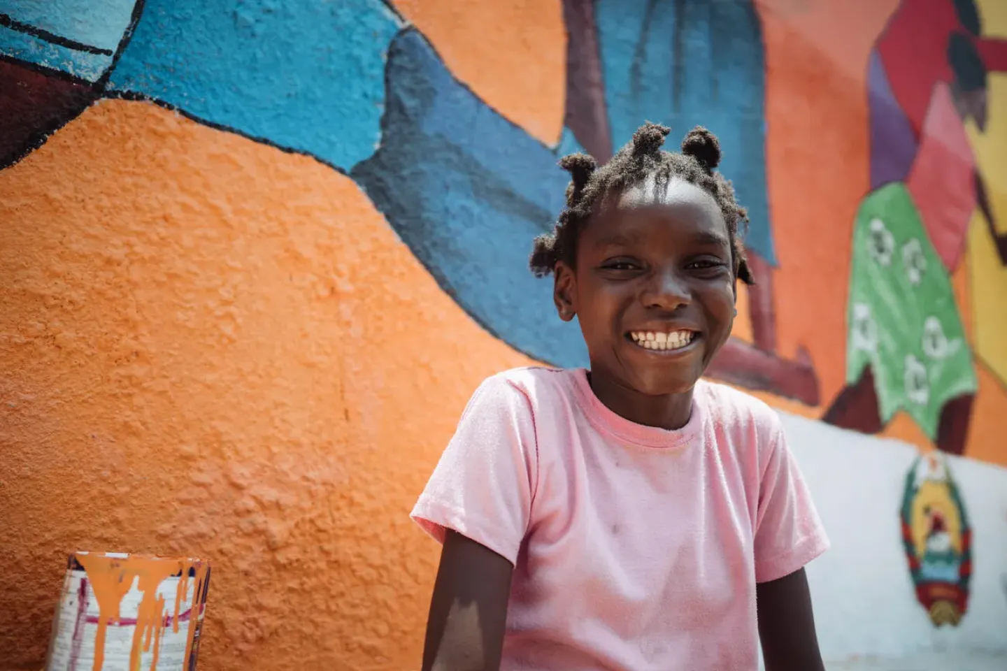A young smiling girl in front of a colourful painted wall