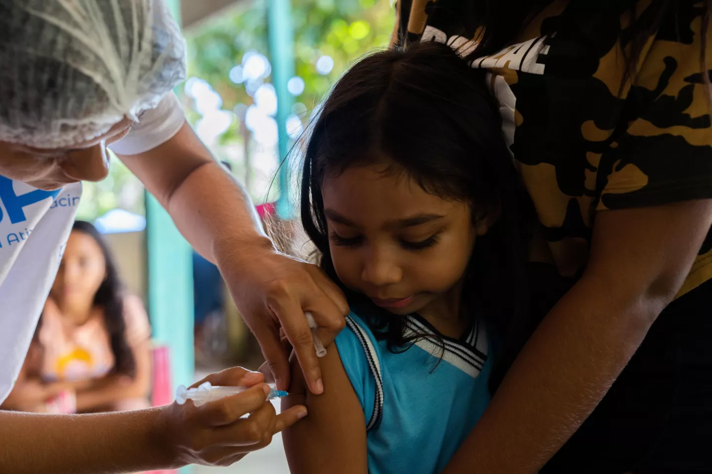 A young girl looks down at her arm while receiving a vaccination.