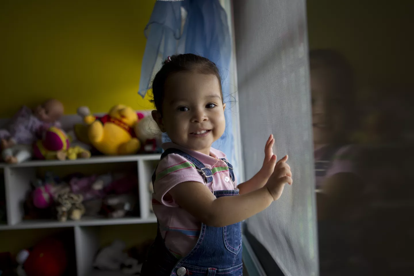 A little girl orphaned by her mother stands, smiling, with her hands on an orphanage window in Panama in 2012.