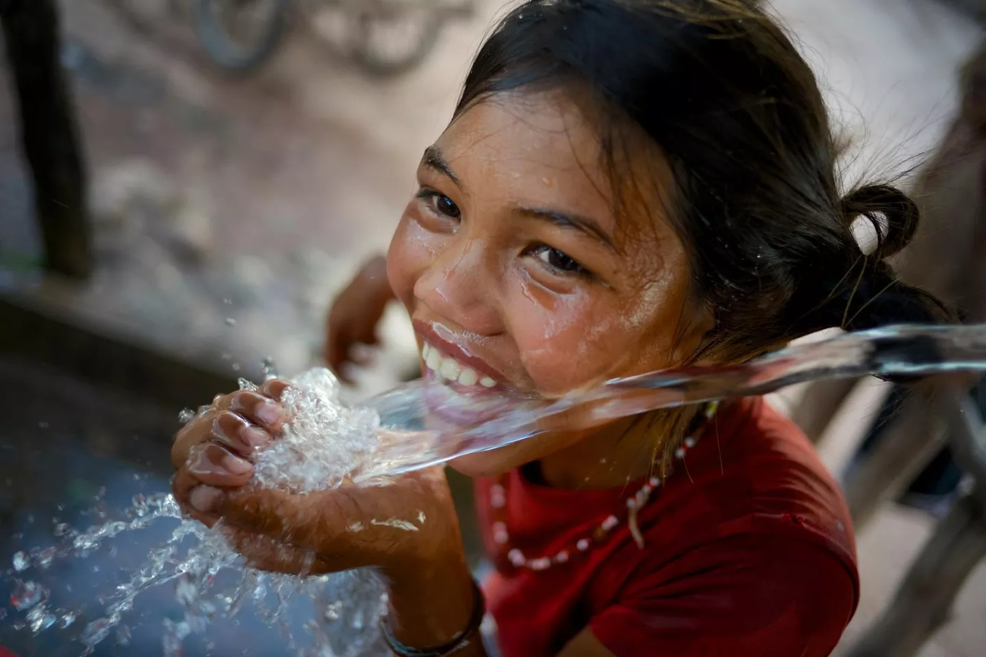 Una ni&ntilde;a se r&iacute;e jugando mientras bebe agua en un punto de agua en el pueblo de Adone del distrito de Ta Oi, provincia de Saravane, RDP de Laos. 