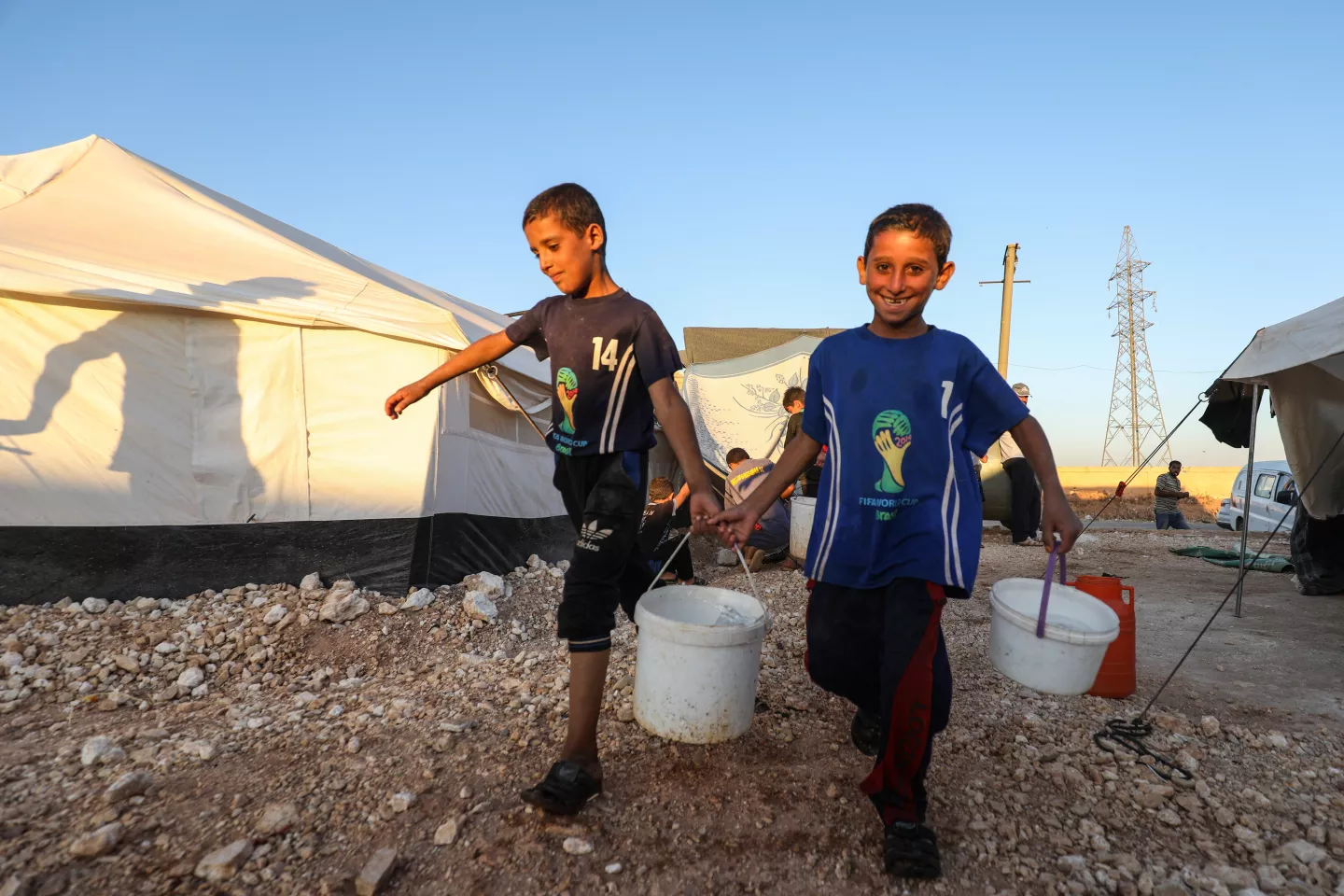 On 24 September 2019 in Idlib in the Syrian Arab Republic, children carry water containers from a tanker to take into the displaced camp near the town of Taftanaz.