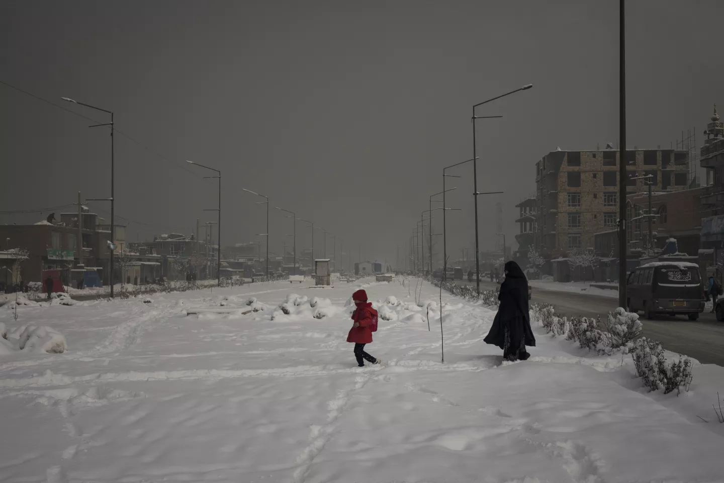 A mother with her daughter walk across a snow covered area of the city during a heavily polluted morning in Kabul, Afghanistan