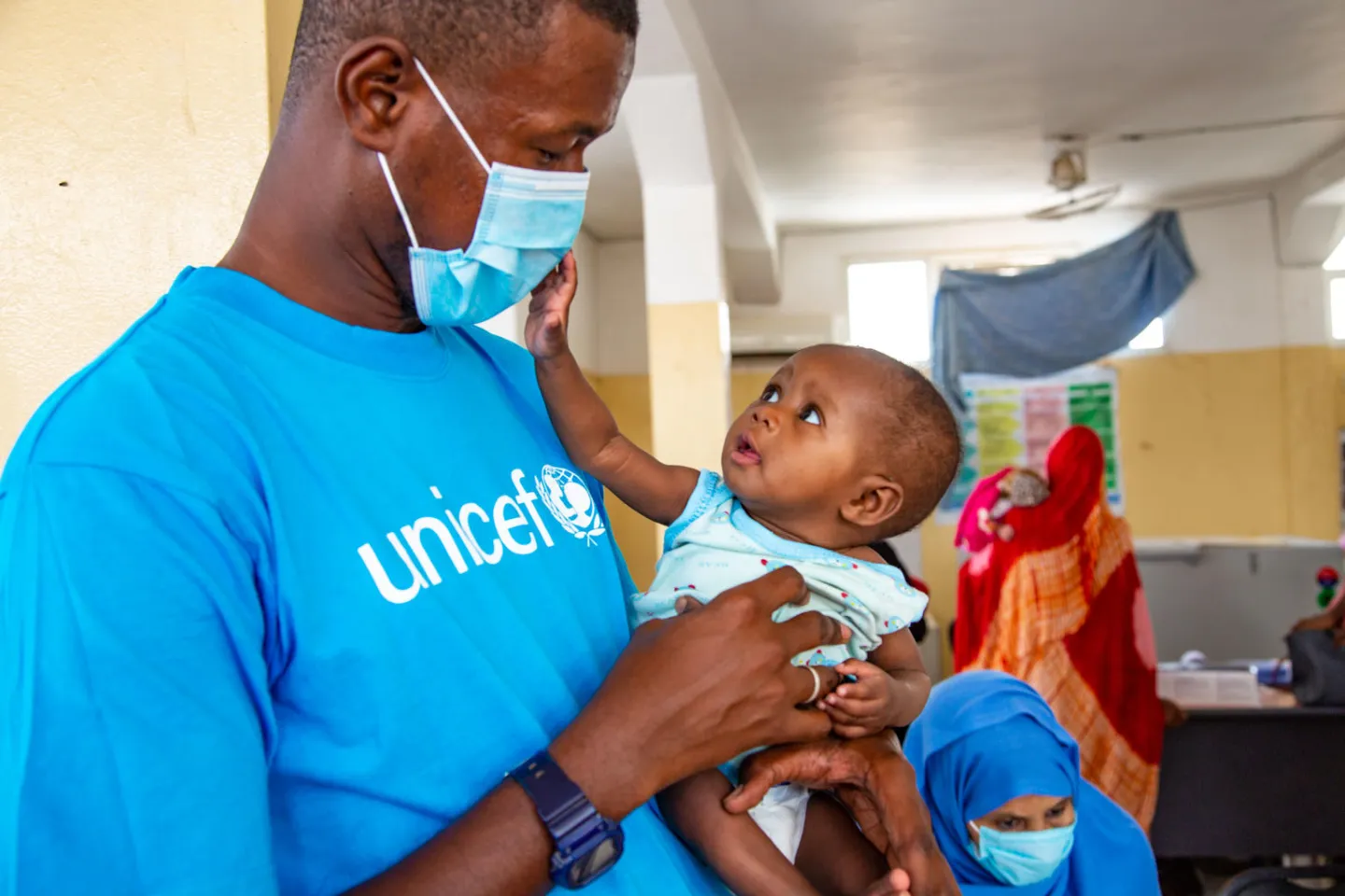 A masked UNICEF nutrition specialist carrying a malnourished baby in the nutrition rehabilitation center of Dar Naim in Nouakchott.