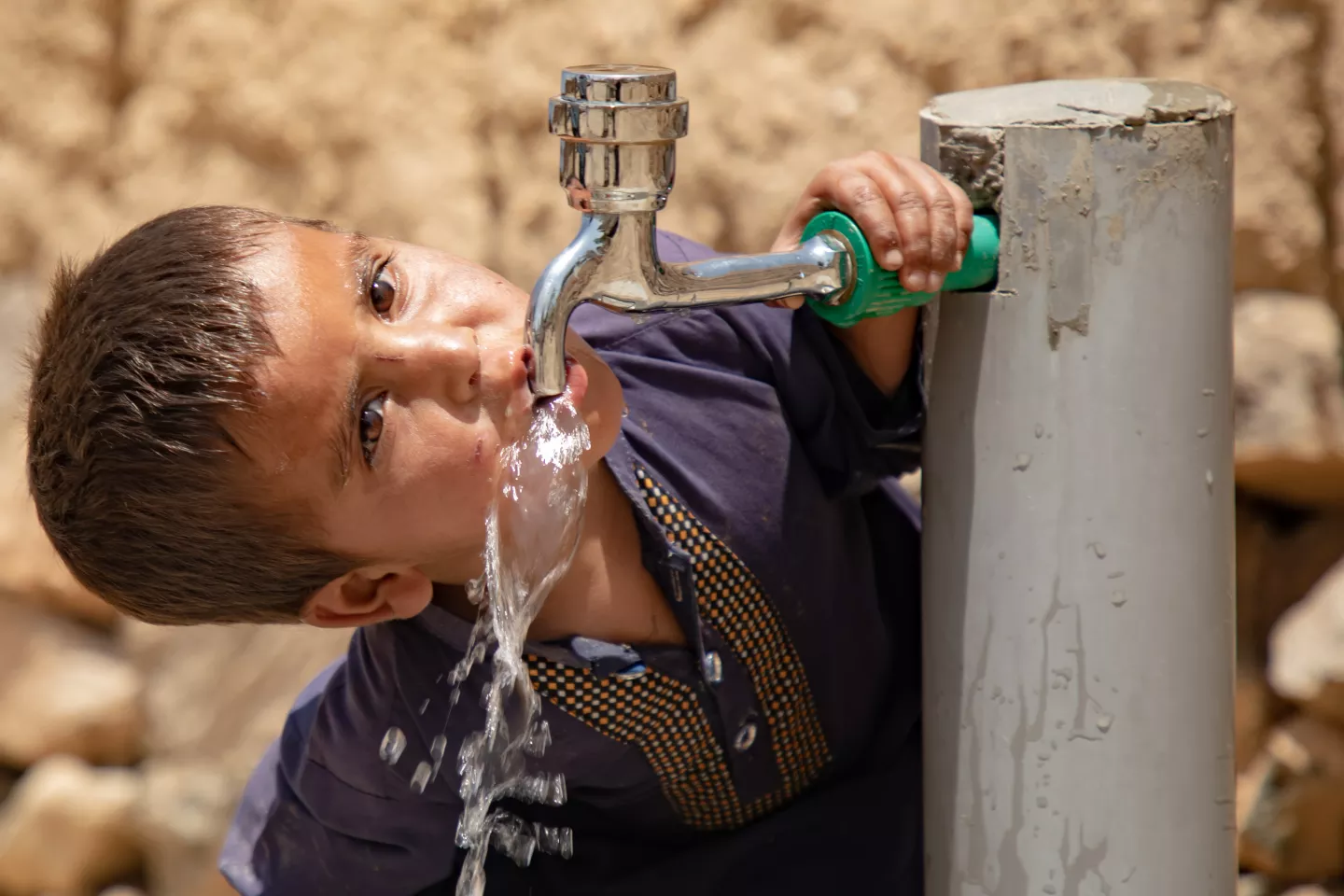 A young boys drinks water directly from a tap.