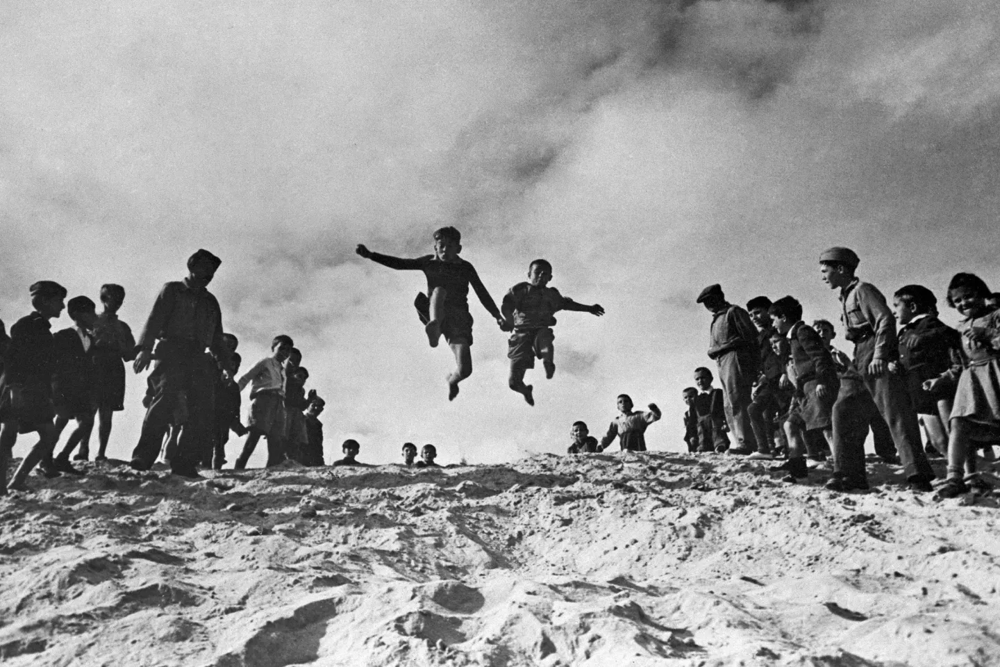 Two boys are cheered on by their companions during the long-jump event of a sports competition at the UNRRA-run El Shatt camp for Yugoslav refugees, near the north-eastern port city of Suez.