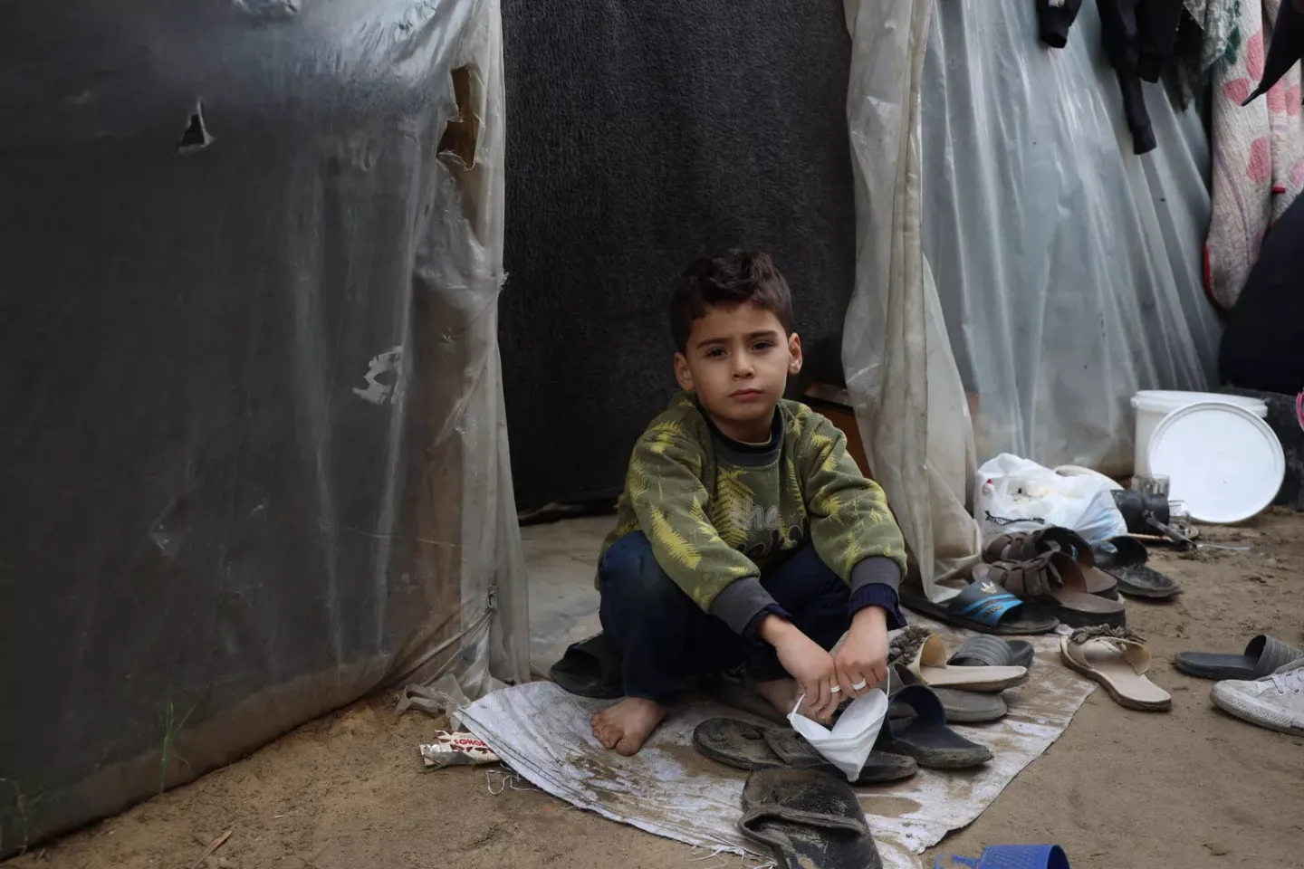 Gaza Strip. A child sits outside a tent at a shelter centre situated within Al-Aqsa University.