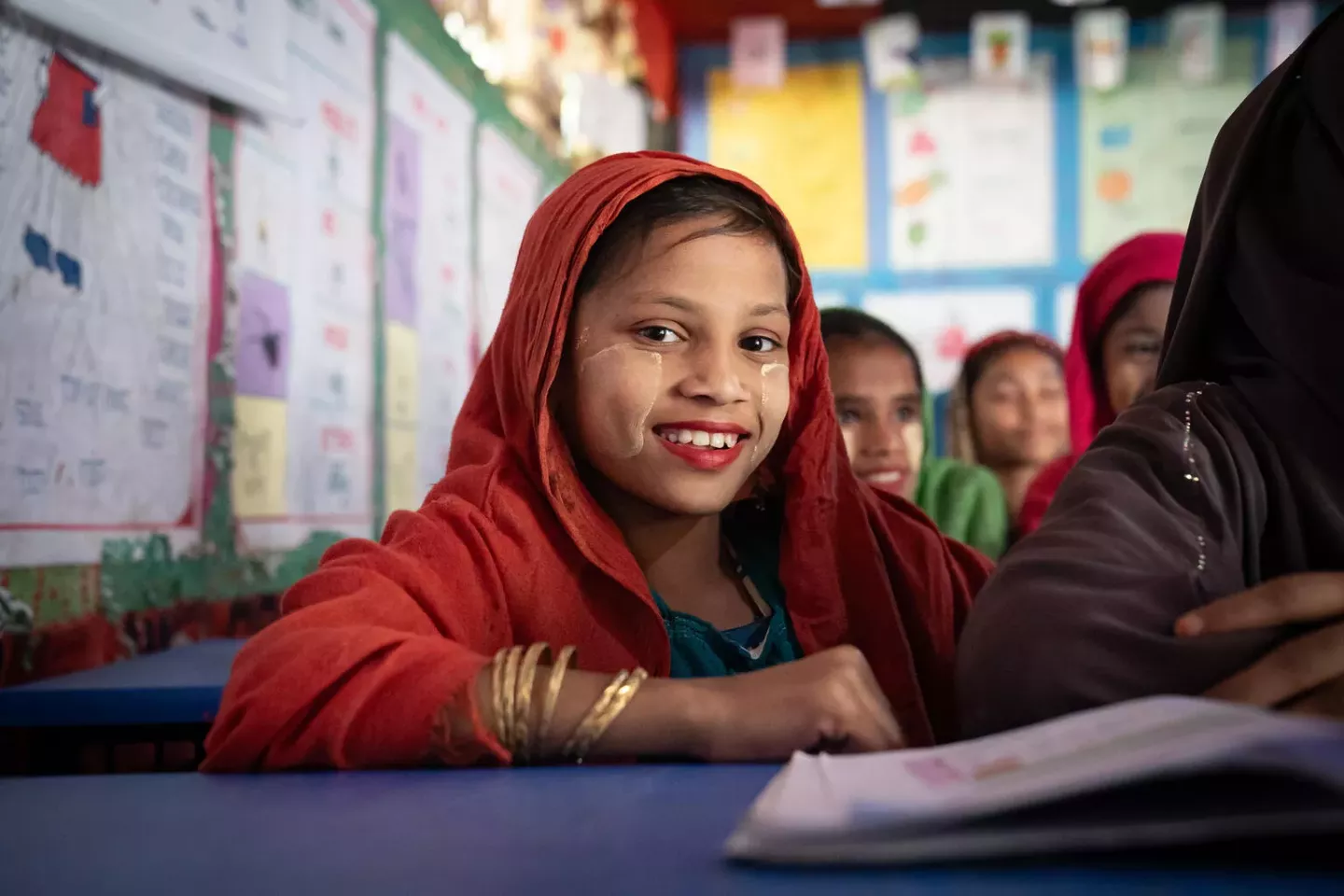 Bangladesh. A girl smiles as she sits at the desk of a UNICEF-supported girls-only learning centre in a Rohingya refugee camp.