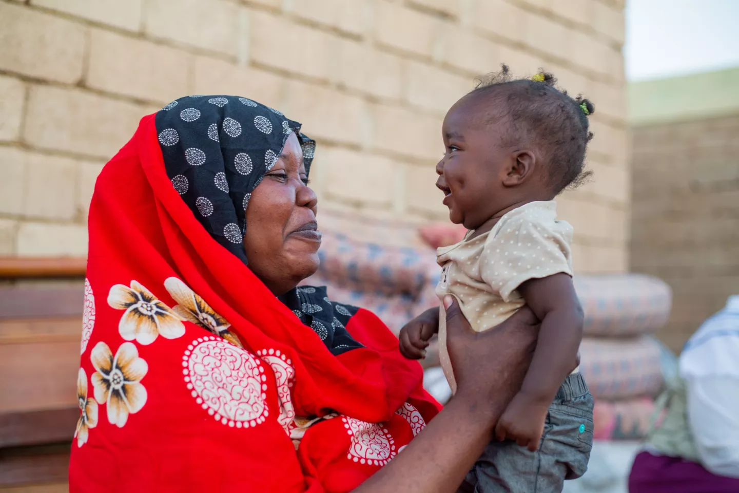 A woman lifts her infant daughter in the air while they smile at each other with joy.