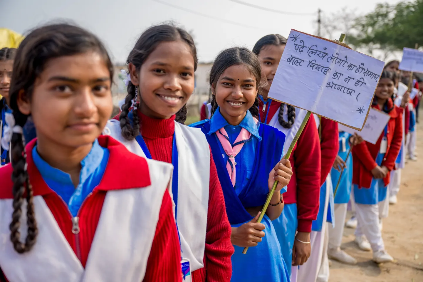 Girls dressed in school uniforms stand in a line with some holding up handwritten placards. 