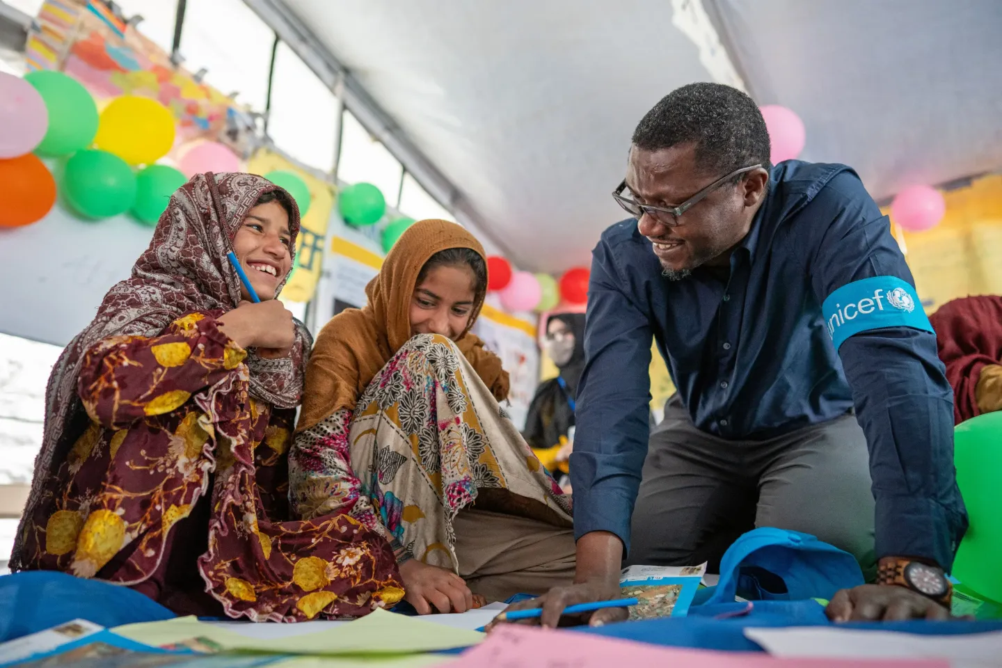 A staff member from UNICEF plays on a classroom floor with two children.