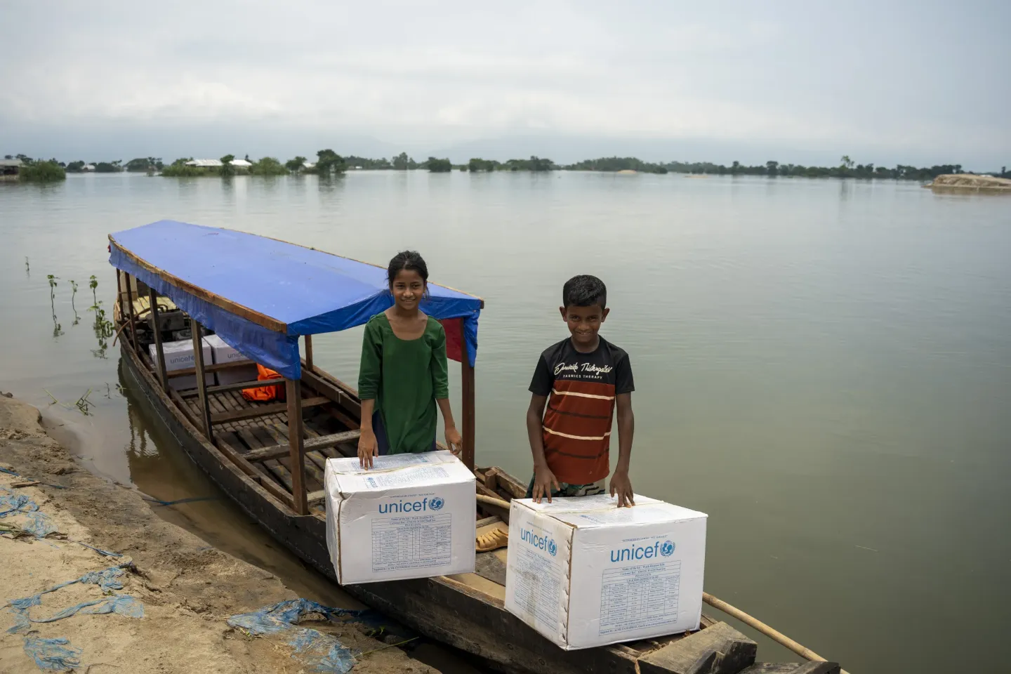An adolescent girl and boy hold UNICEF nutrition kits in their wooden boat after Bangladesh floods.
