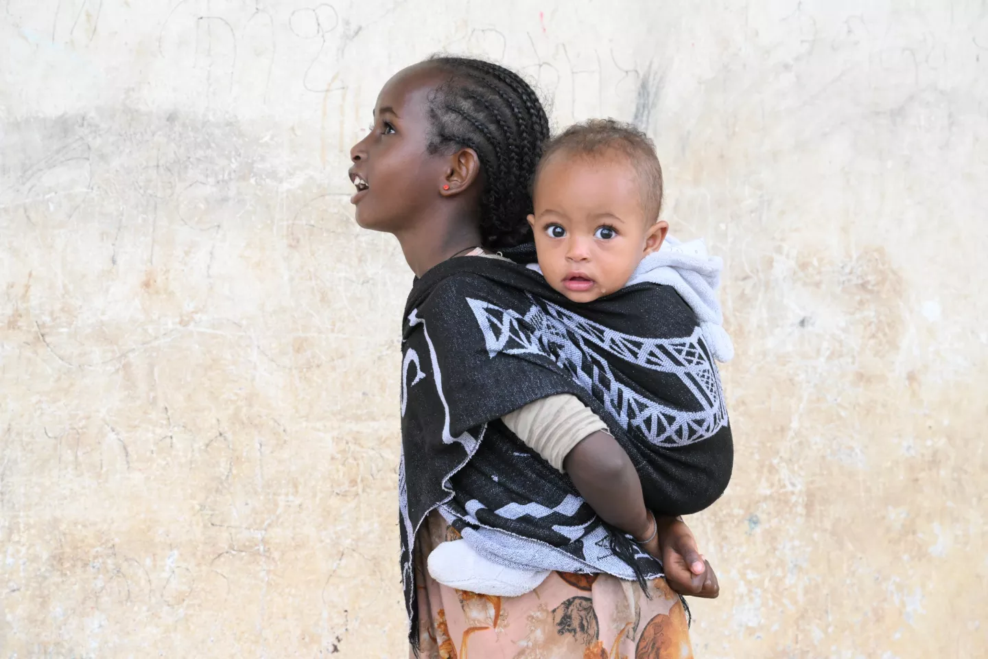 Une jeune fille porte son petit fr&egrave;re ou sa petite s&oelig;ur sur son dos.
