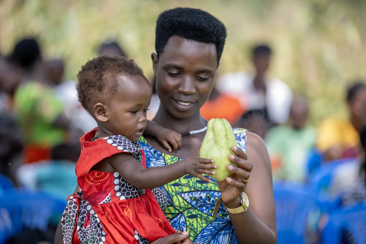 Musimenta Agnes holds a chayote squash fruit to her one-year-old daughter Atuhaire Provia at a community gathering showcasing the benefits of a community-led, UNICEF-supported initiative to combat malnutrition in western Uganda.