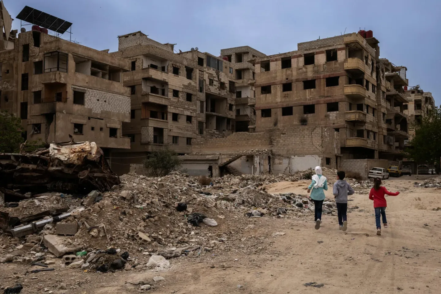 Syria. Three children run along a street past badly damaged buildings in Ain Tarma.