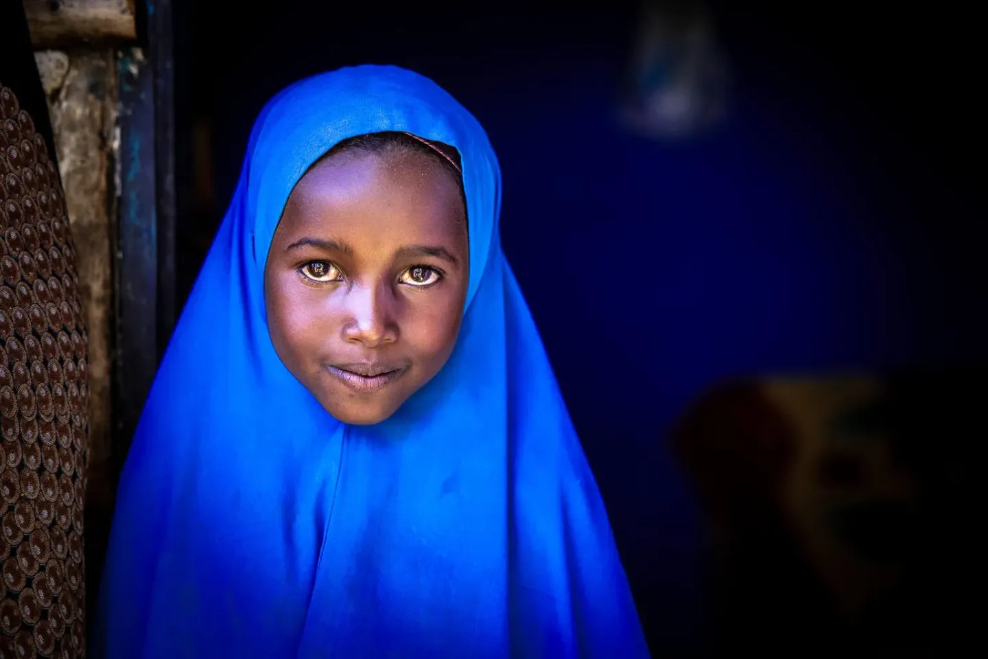 An eight-year-old girl poses for a portrait in a vibrant blue head scarf.
