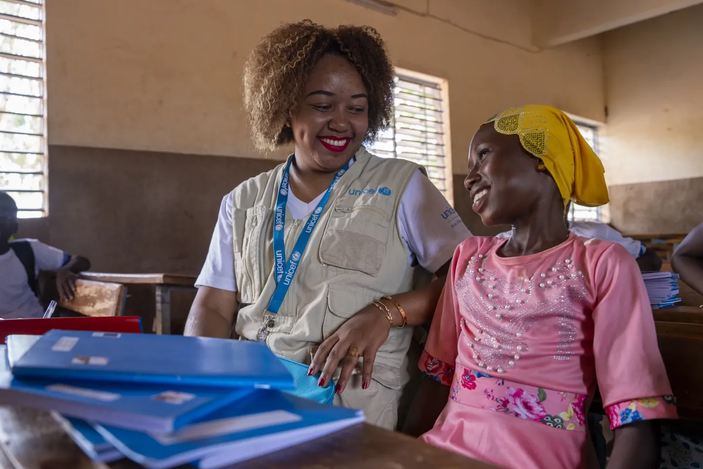 A UNICEF staff member sits with a smiling child in a classroom. 