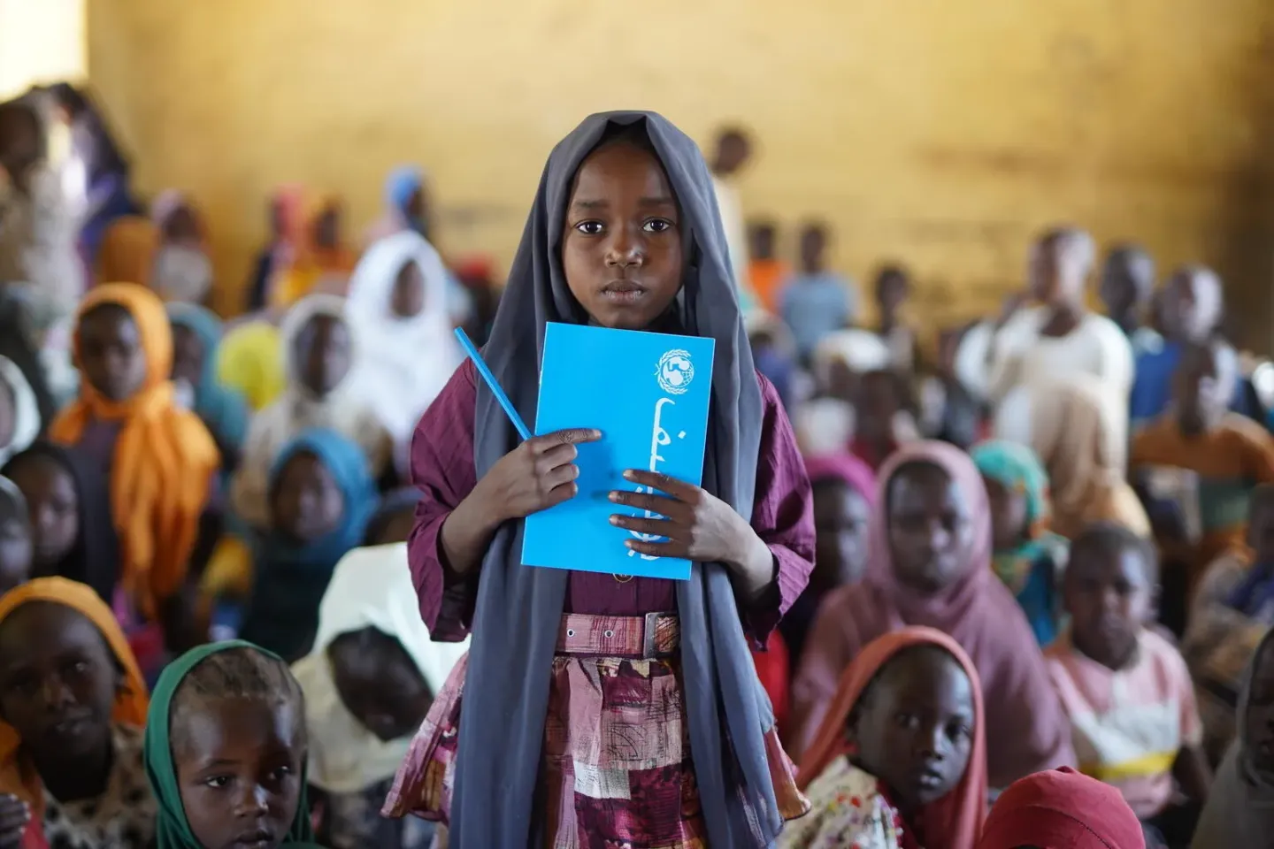 Sudan. A girl holds a notebook as she stands in front of classmates.