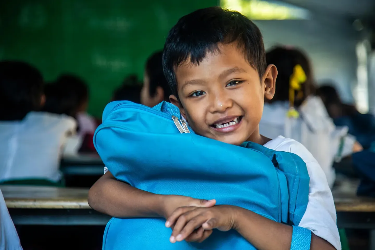 Myanmar. A boy hugs a backpack in a tent classroom being used as temporary learning spaces after an earthquake damaged classrooms and school buildings in Mandalay Region.