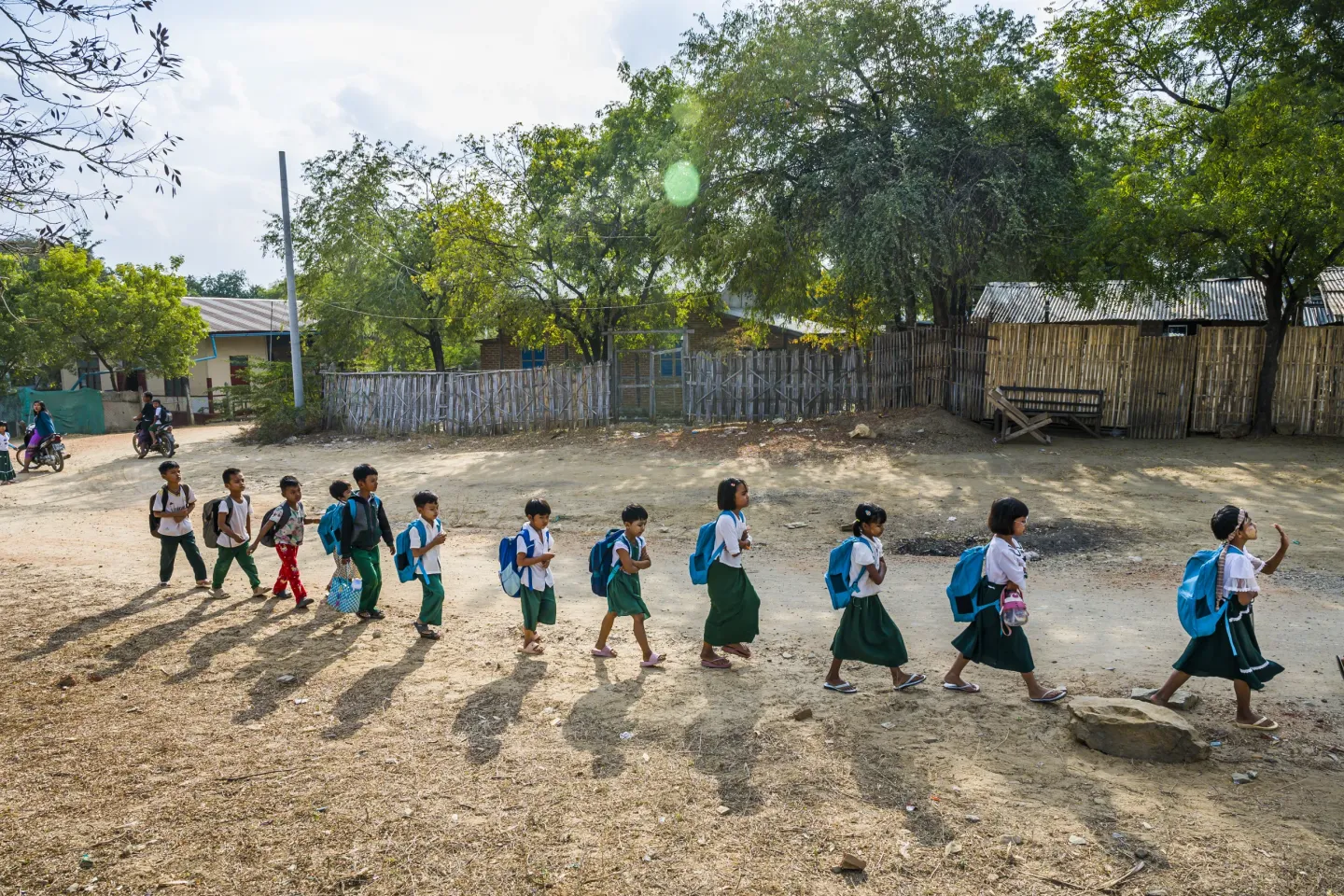 A group of children walk in a line from school wearing blue UNICEF backpacks.