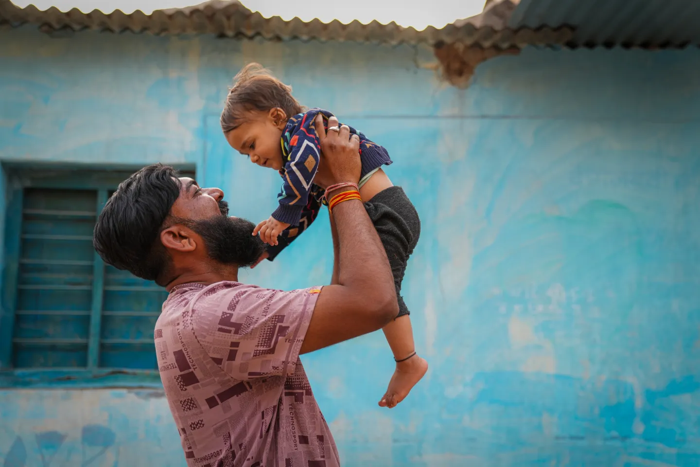 A father joyfully with his one-year-old daughter Khushi into the air outside their home.