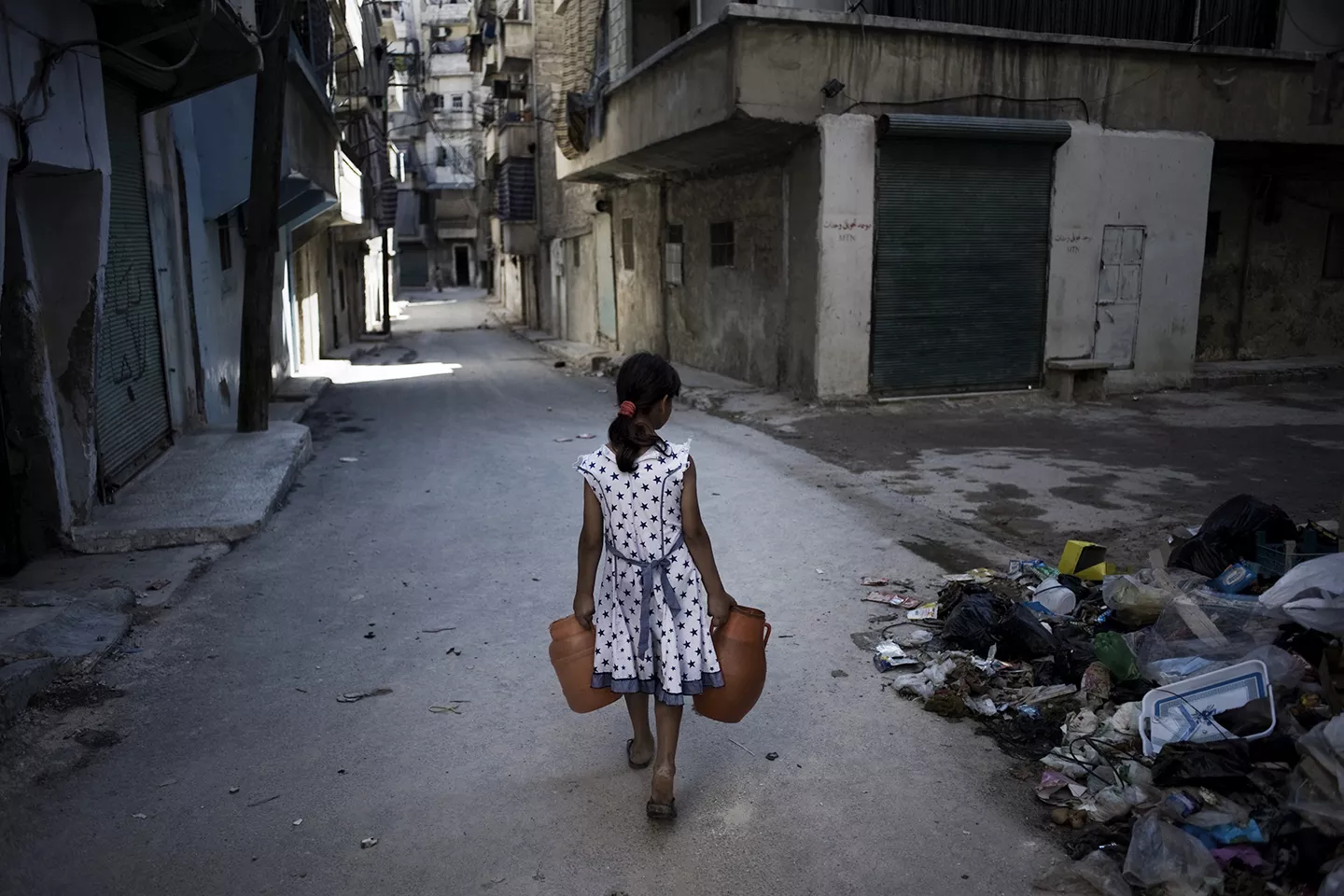 A girl on a street in Aleppo, carrying jerrycans of water