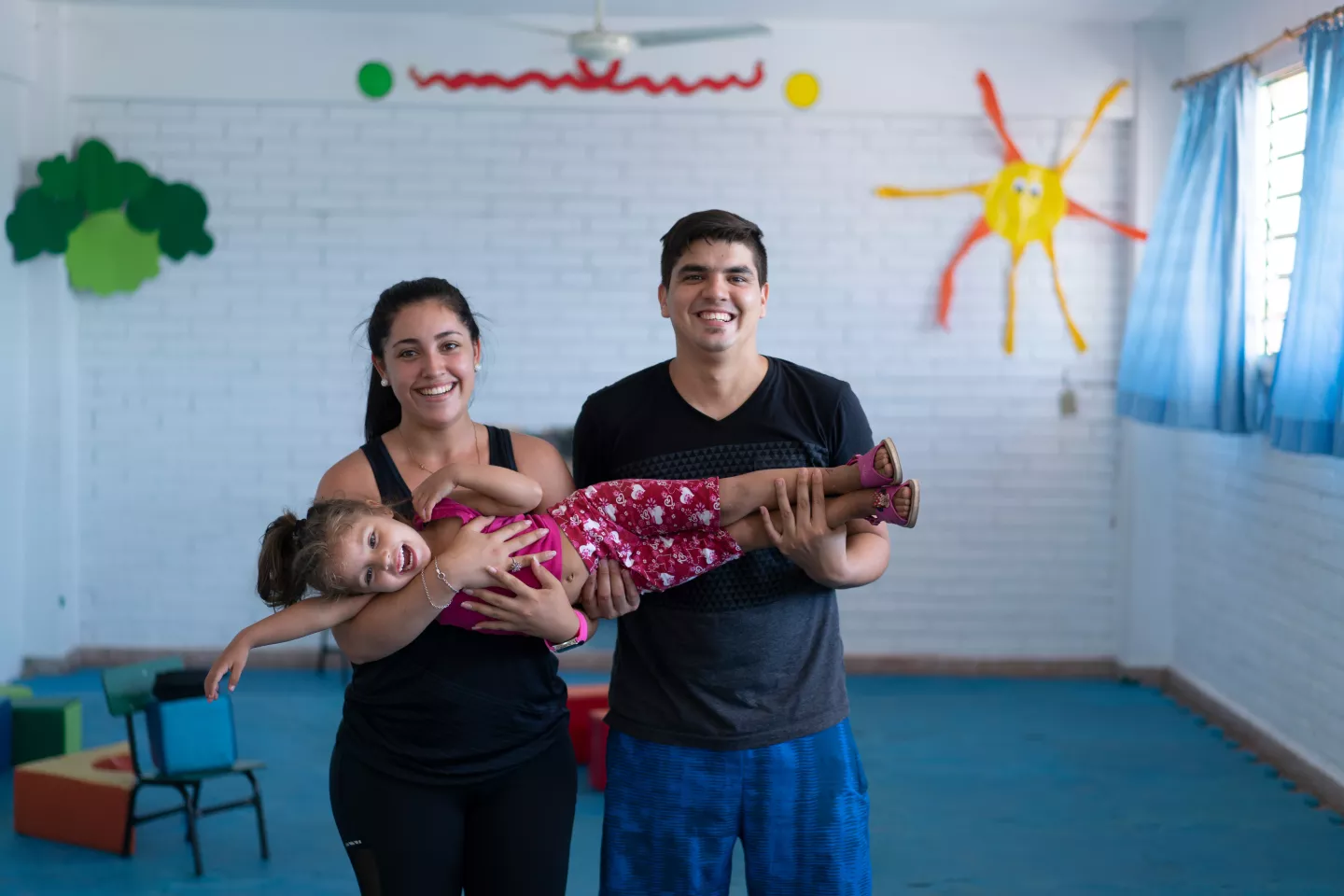 A smiling child flailing happily in the arms of her parents