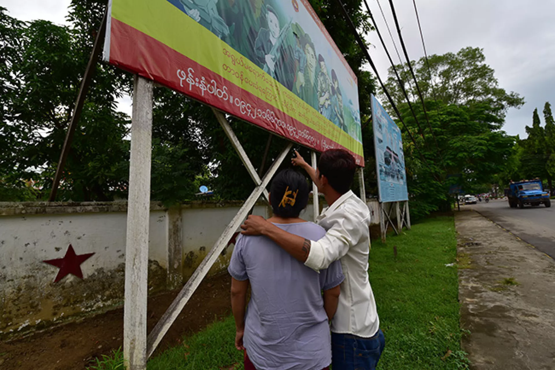 Zwe Chit and his mother look at the child recruitment prevention billboard and point at the hotline number. 