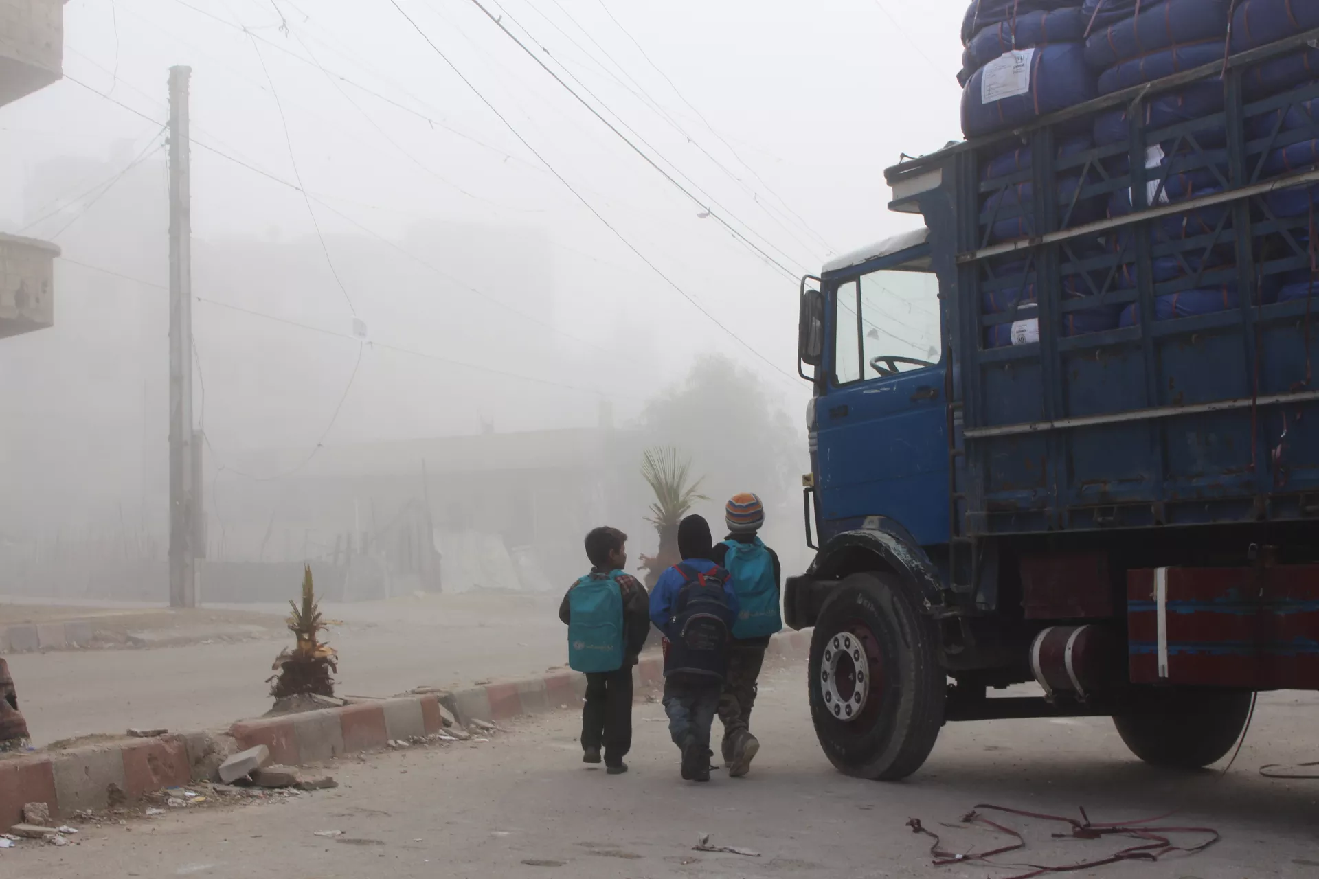 Children in backpacks stand next to a truck