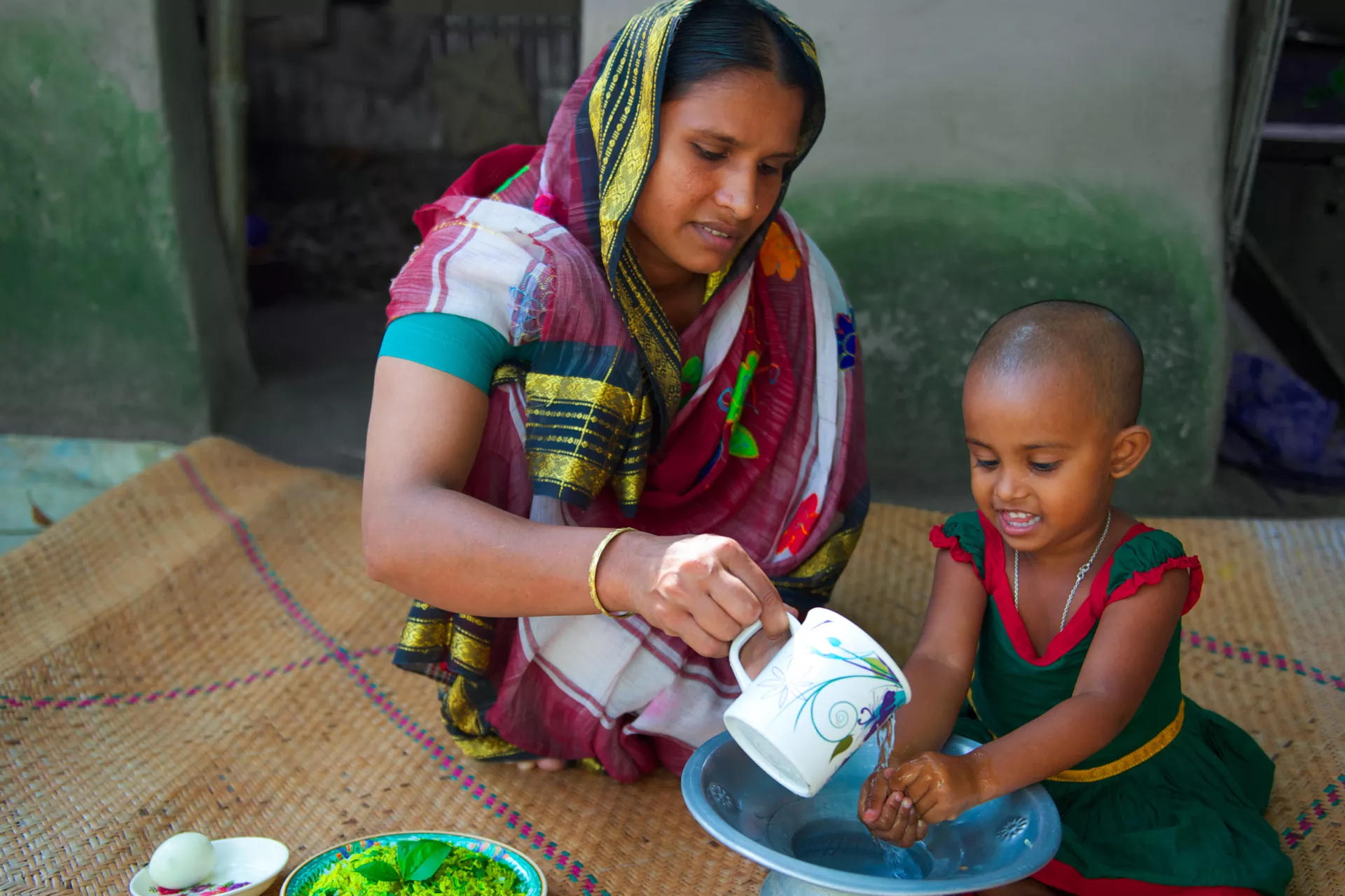 A mother pouring water on her child's hands to wash them