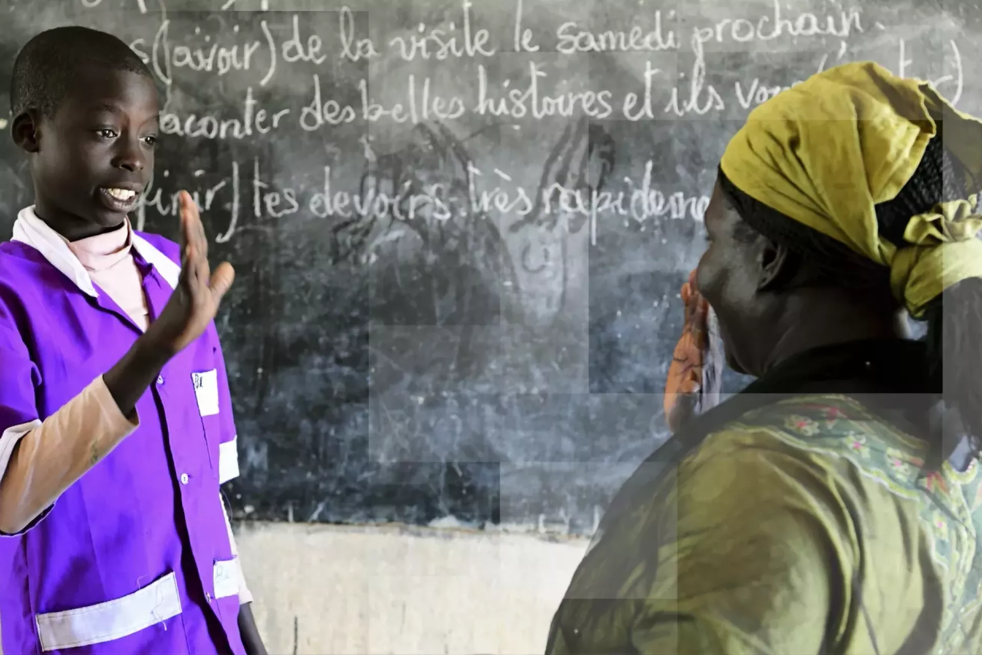 A boy and his teacher stand in front of a blackboard about to give each other a high 5