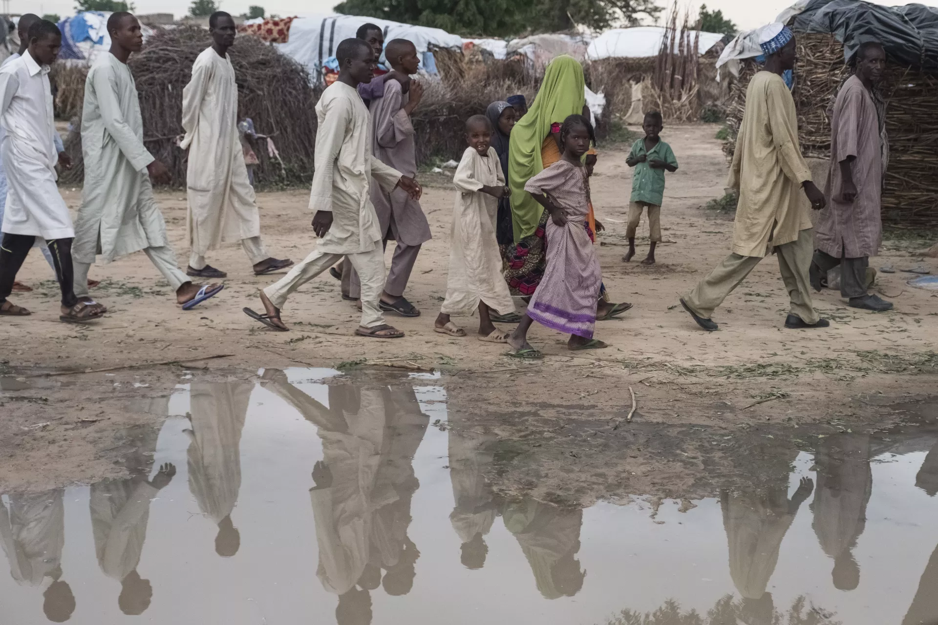 Displaced people walk around a puddle in Shuwari 8 camp, in Medinatu, Borno State, Nigeria