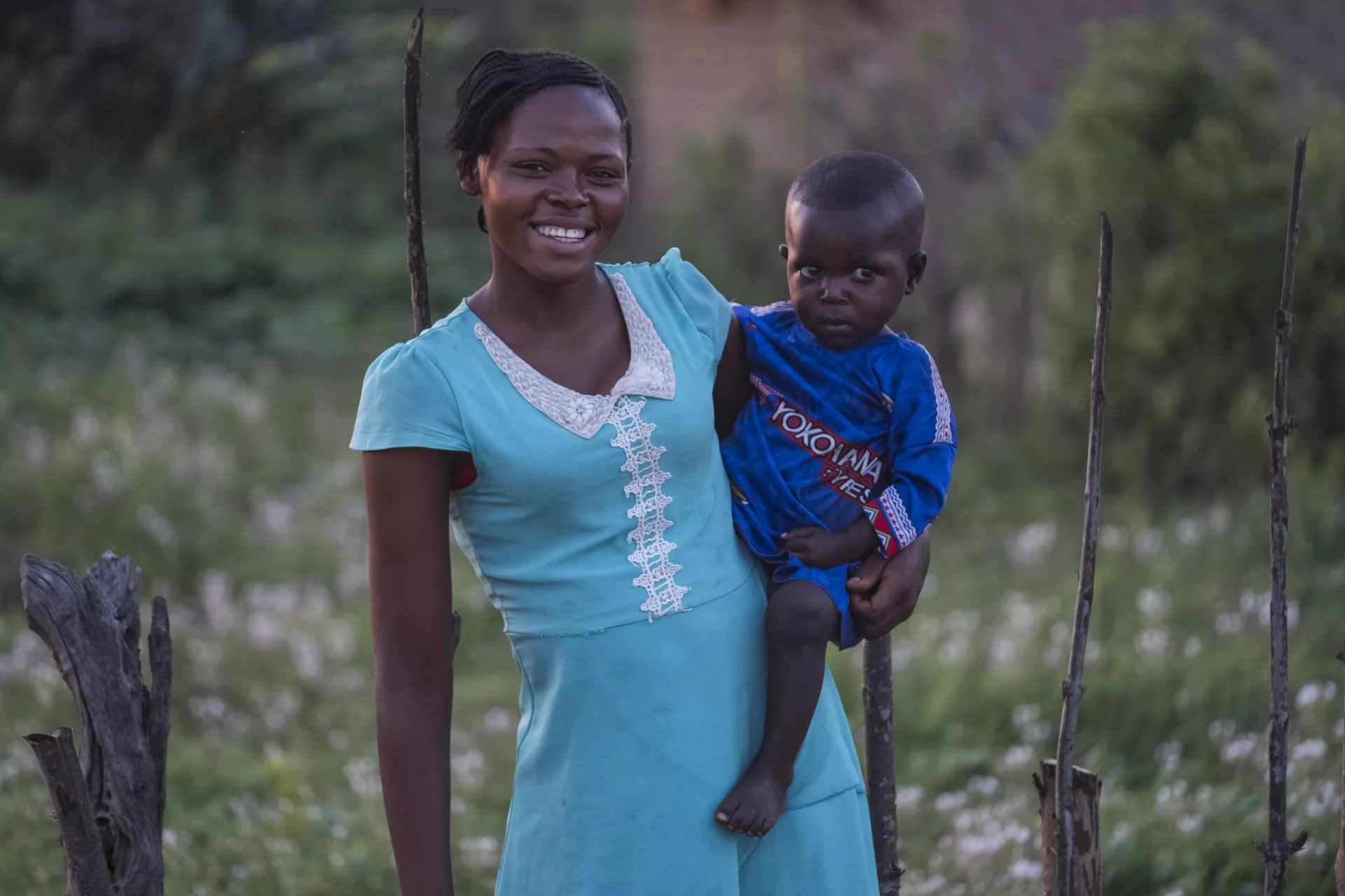 An adolescent girl smiles as she carries a young boy on her hip.