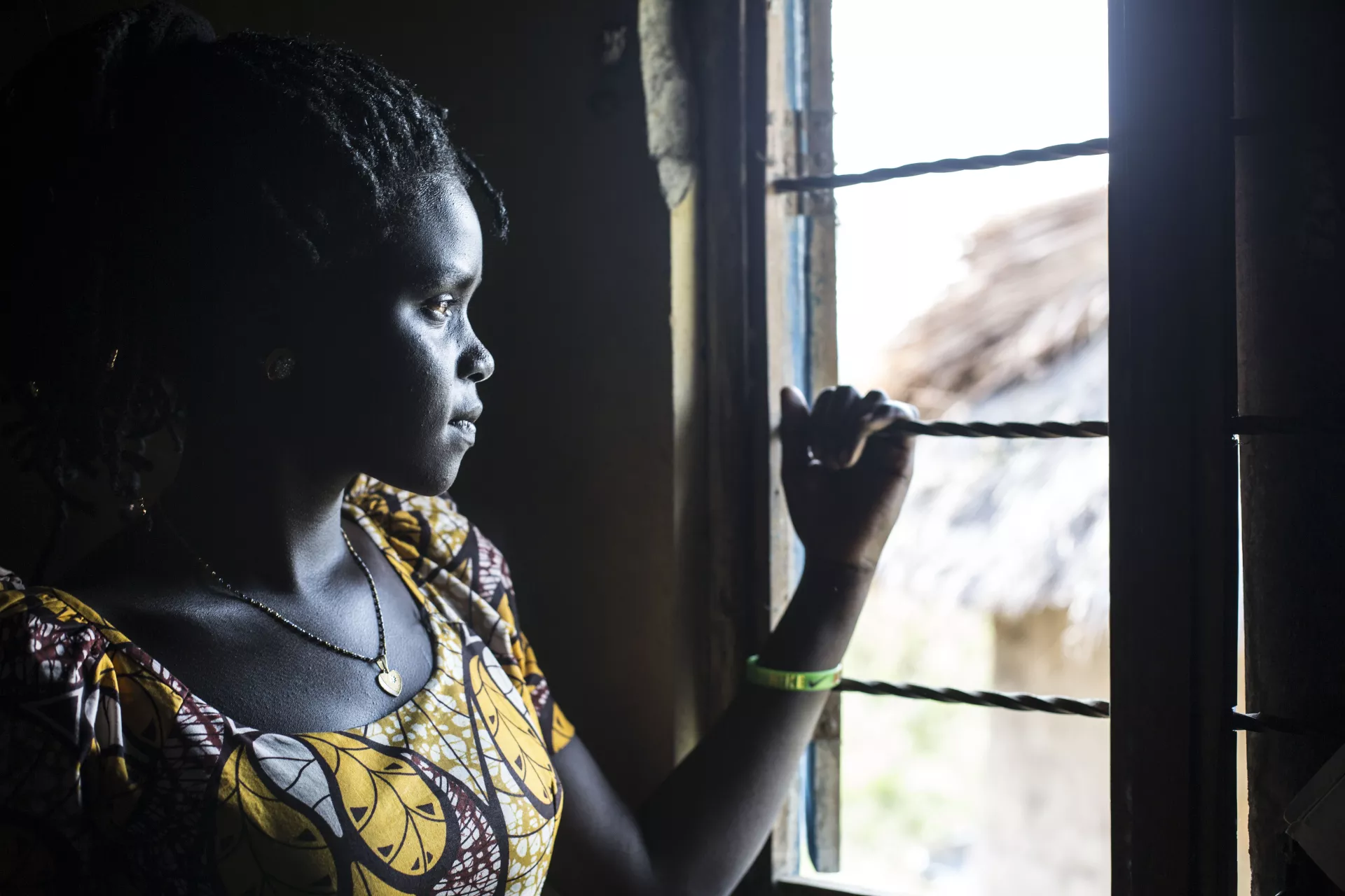 A young woman looks out the window of her home in Uganda.