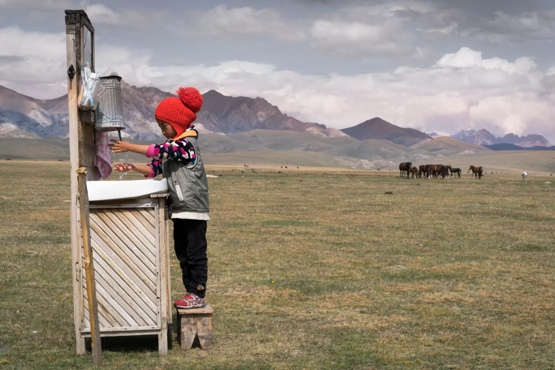 Ainazik Nurmambetova shows us her hand washing practice as a daily routine using the outdoor basin complete with a mirror, step stool, soap, toothbrush, and cupboard.