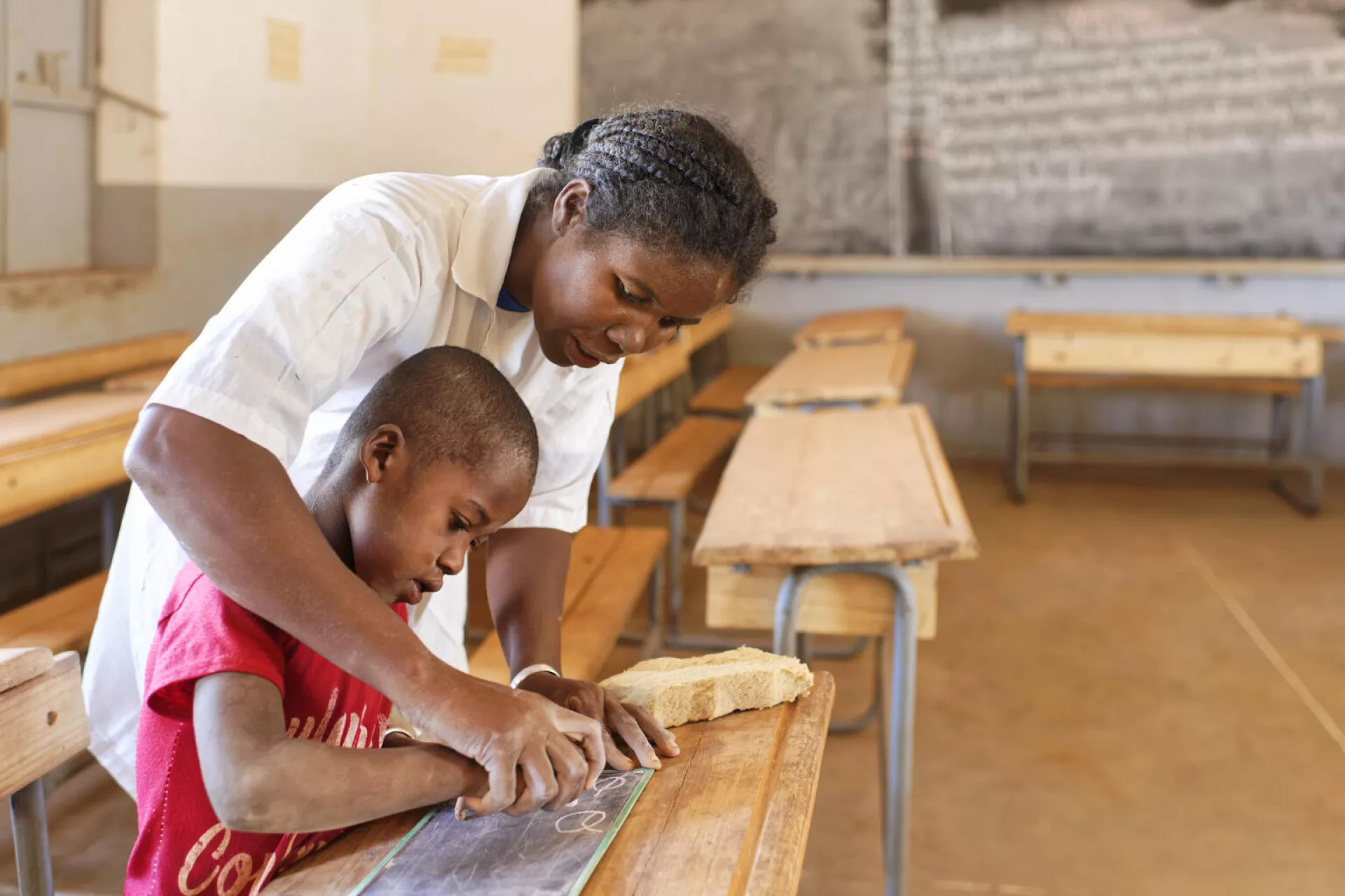 On 18 August 2021, in Ambovombe, Madagascar, a teacher helps a child writes the vowels on a small blackboard at Beabo Primary school.