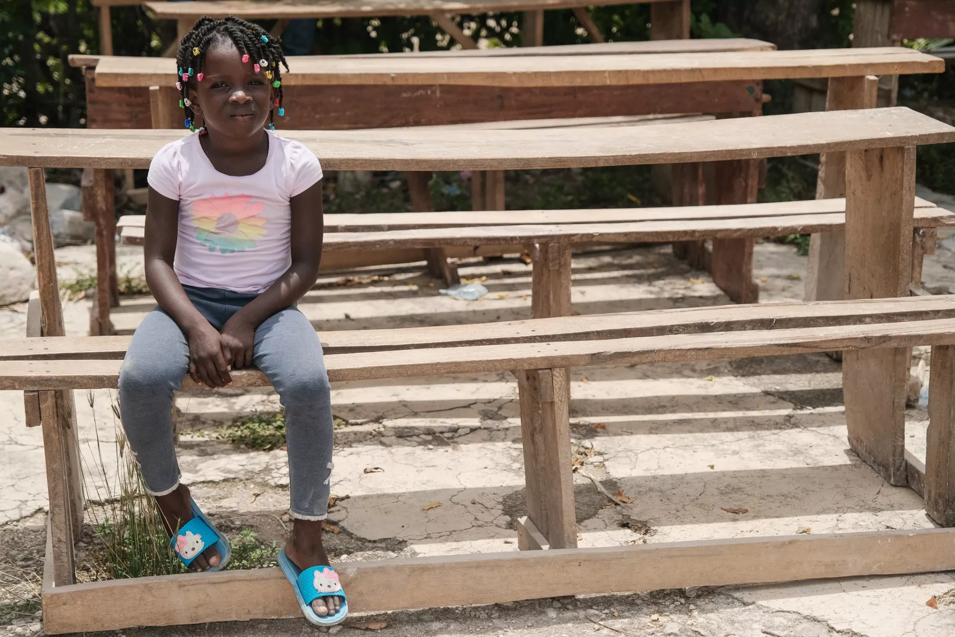 Haiti. A child sits on a bench outside a destroyed school.