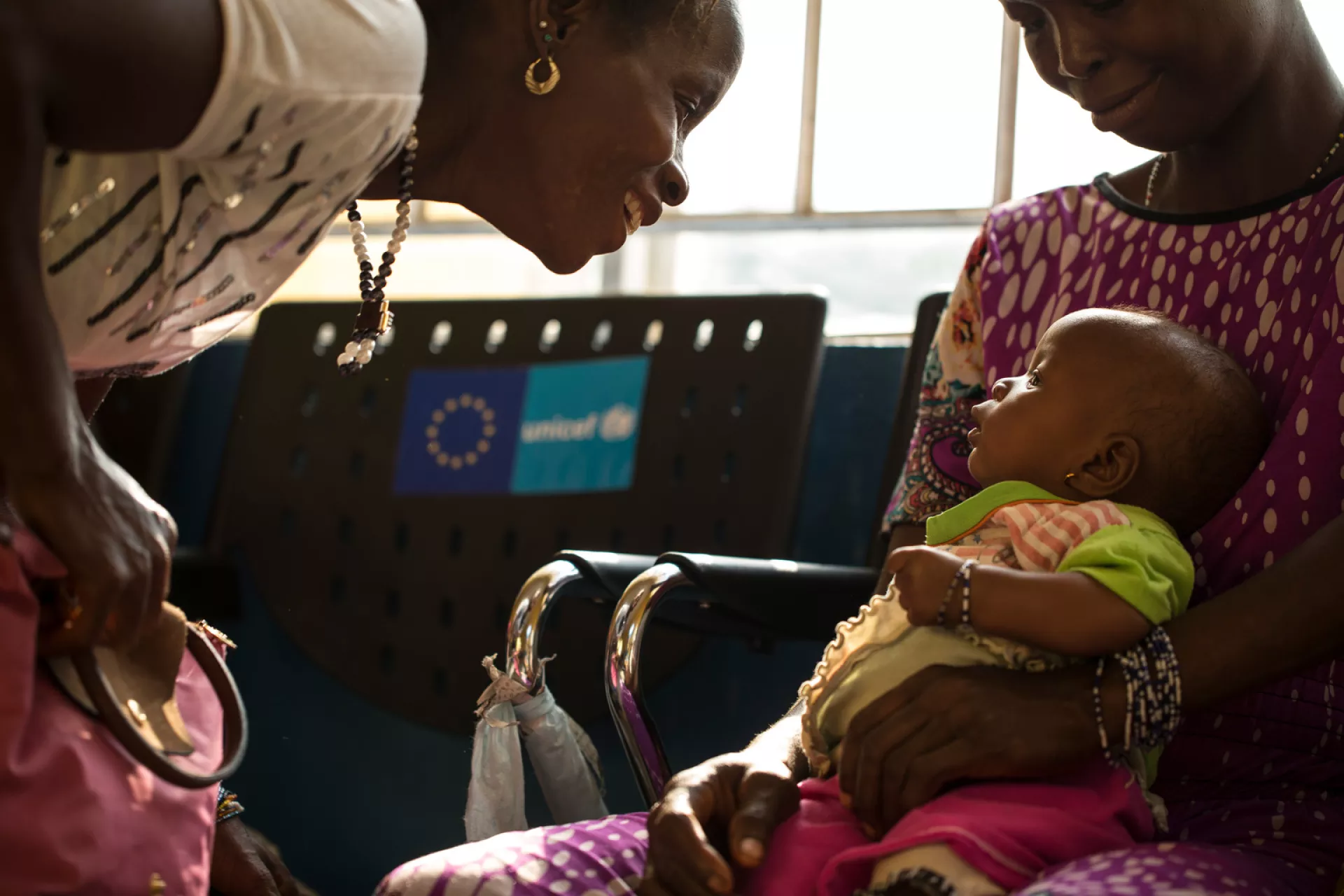 A woman plays with a baby girl in the lap of another young woman. 