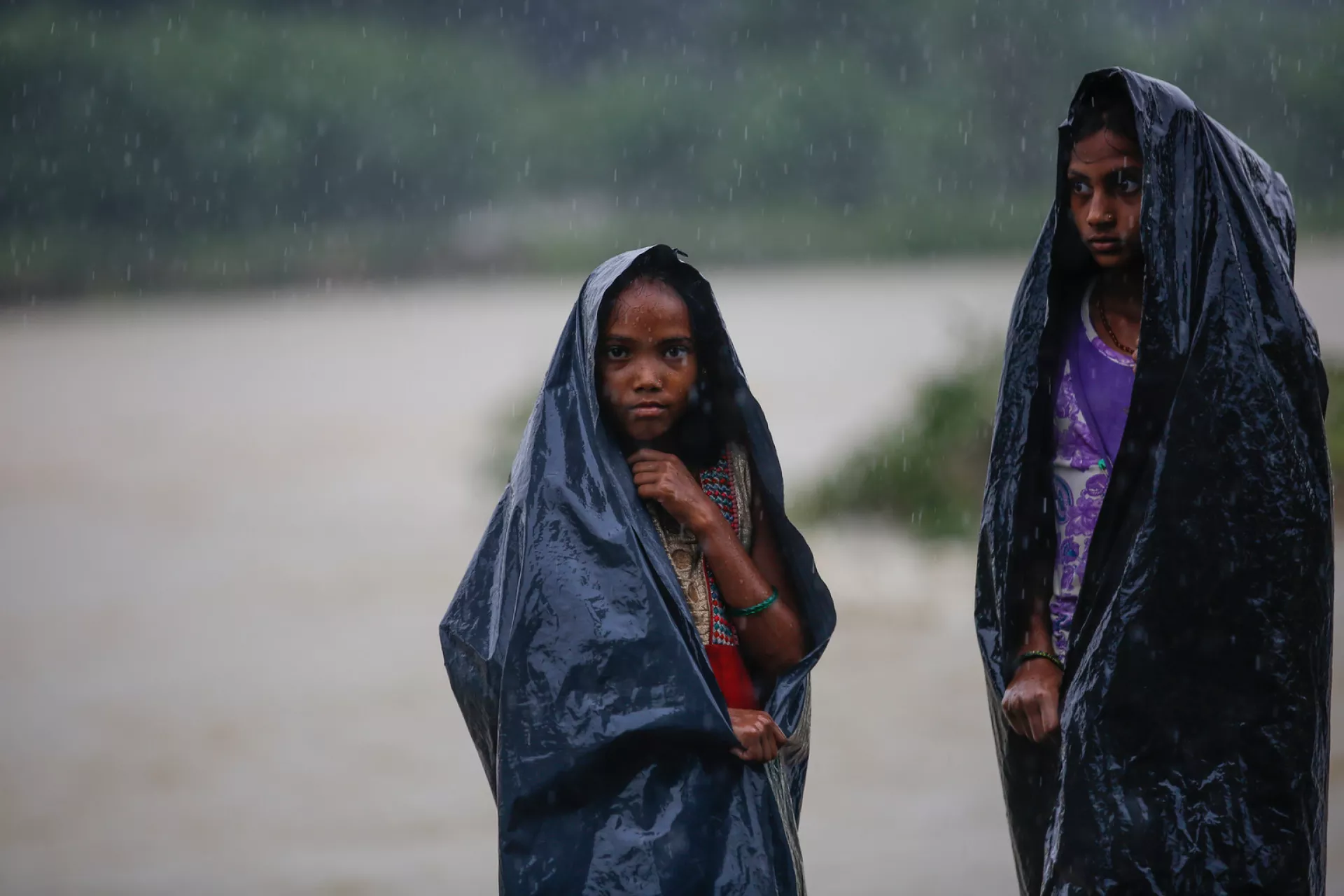Two girls use plastic sheets to hide from the rain in Nepal