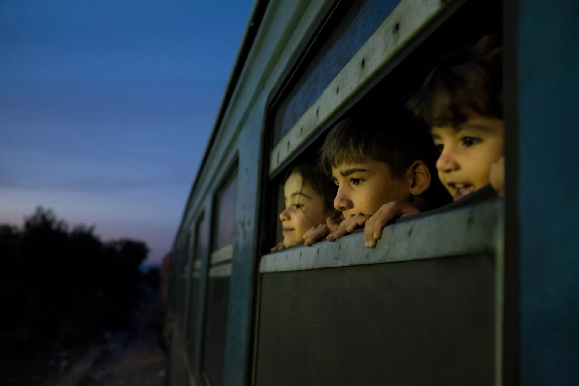 Three children look out of the window of a train as refugees primarily from the Syrian Arab Republic, Afghanistan and Iraq board the train at a reception center for refugees and migrants, in Gevgelija.