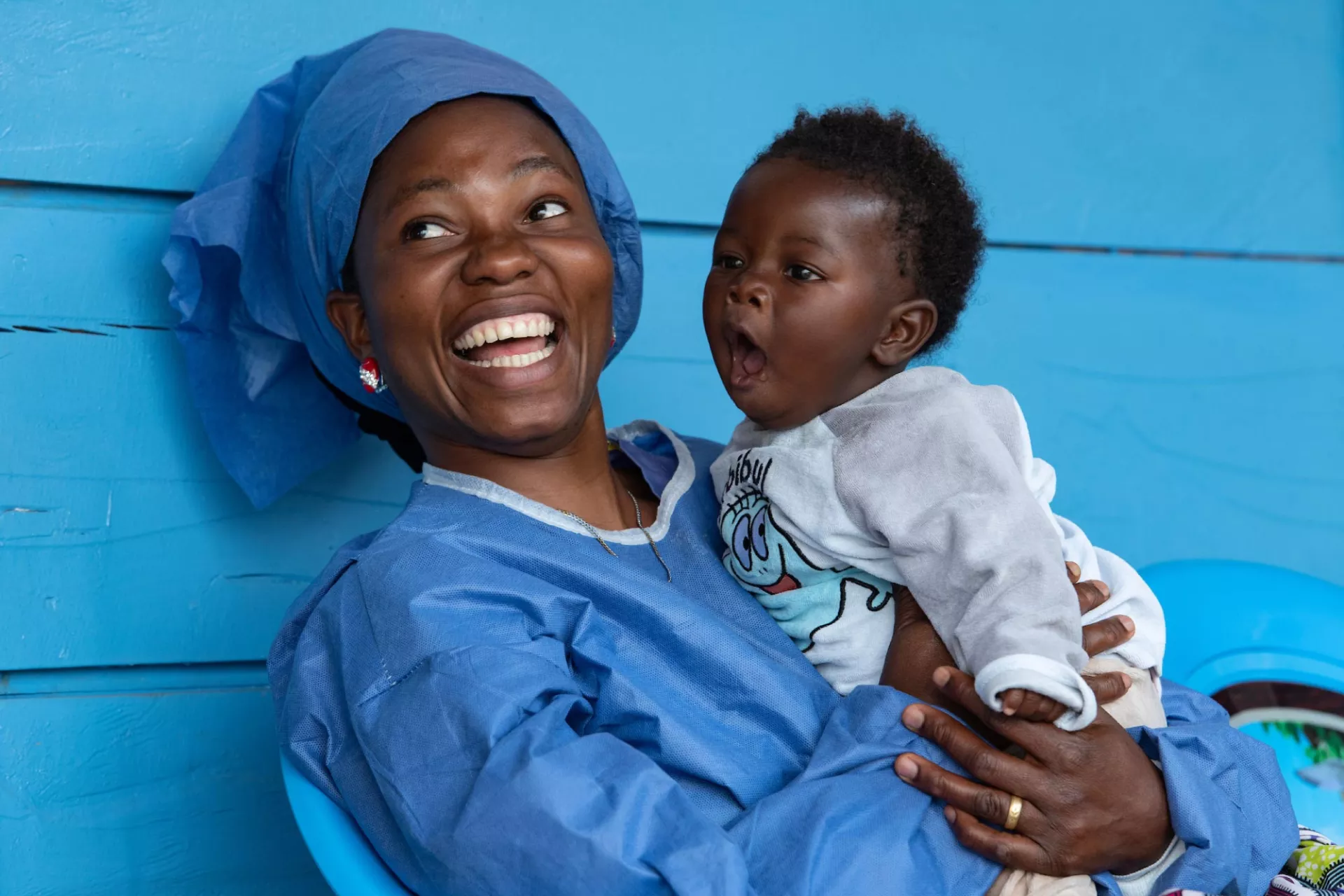 A woman dressed in blue smiles with a young baby sitting on her lap