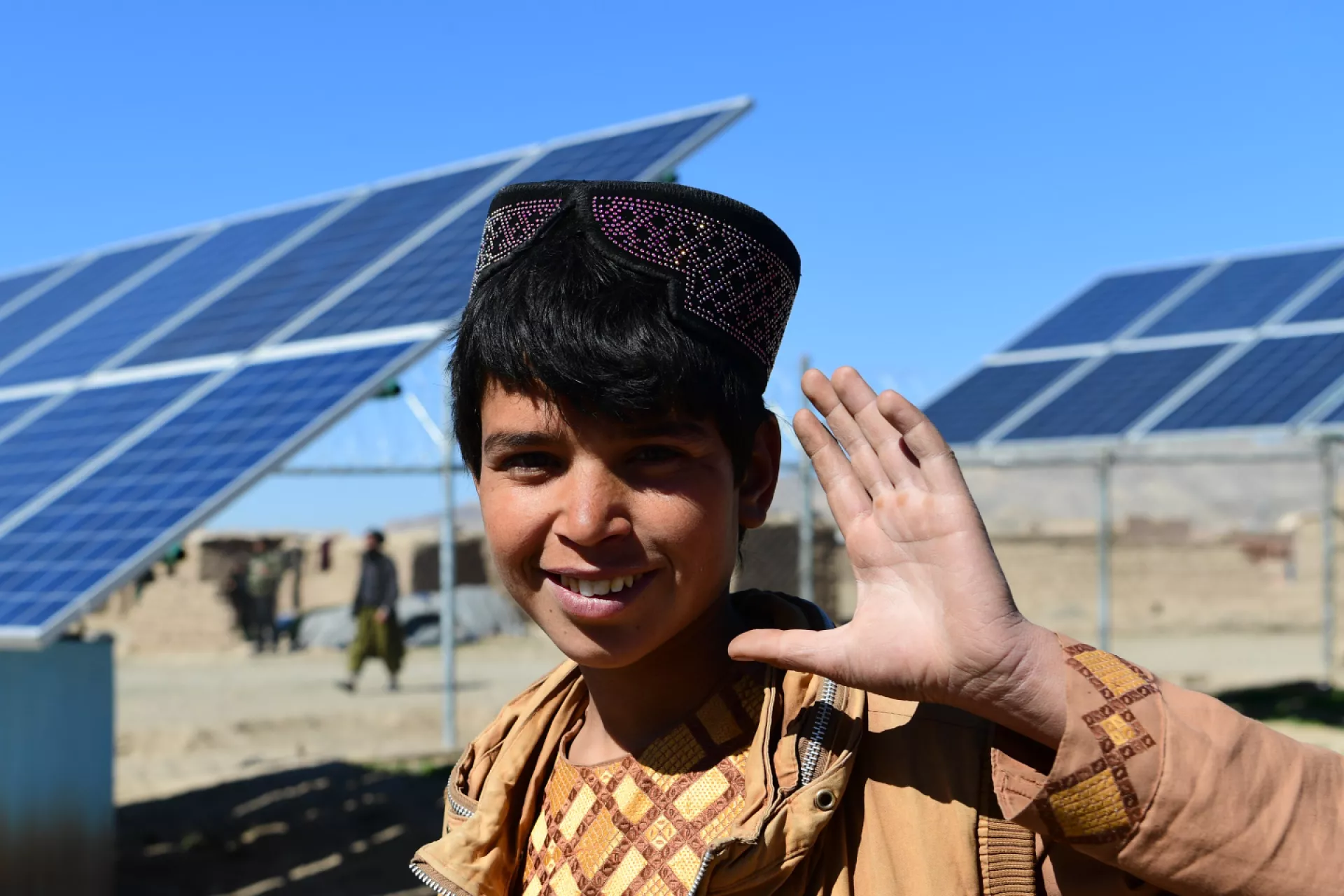 A boy standing in front of solar panels and waving