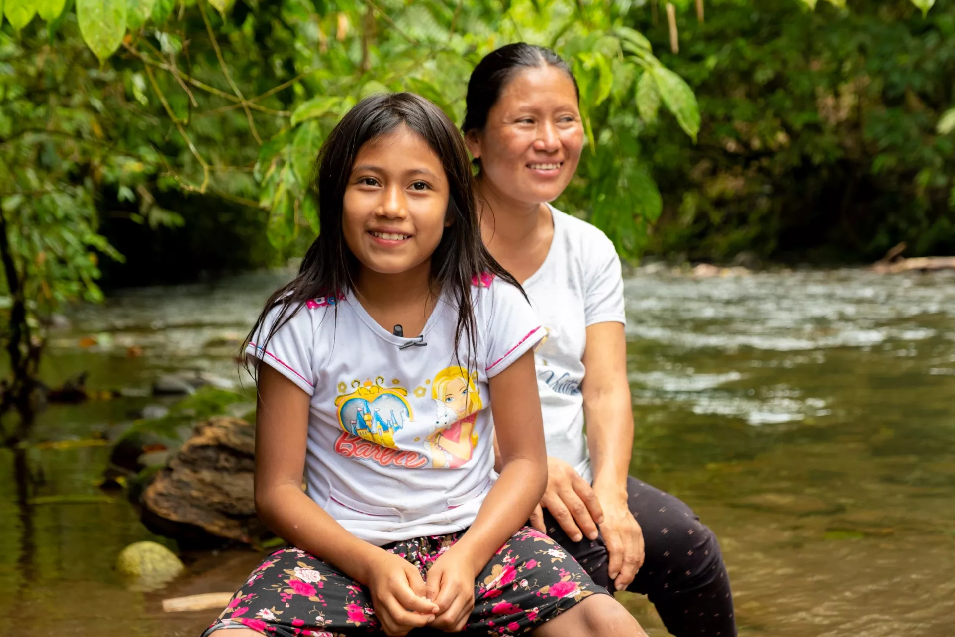 Ecuador. A girl sits with her mother near a river.