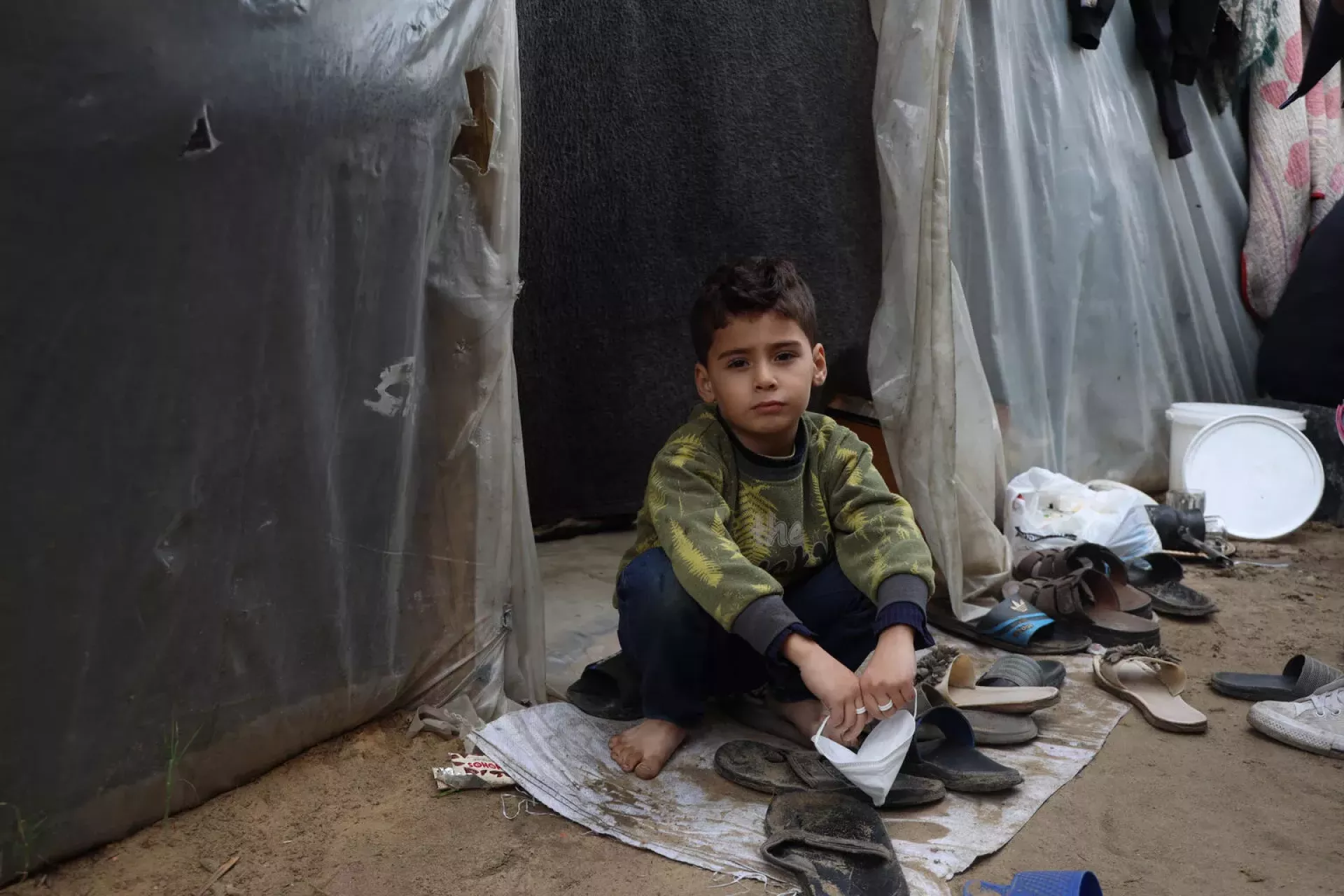 Gaza Strip. A child sits outside a tent at a shelter centre situated within Al-Aqsa University.