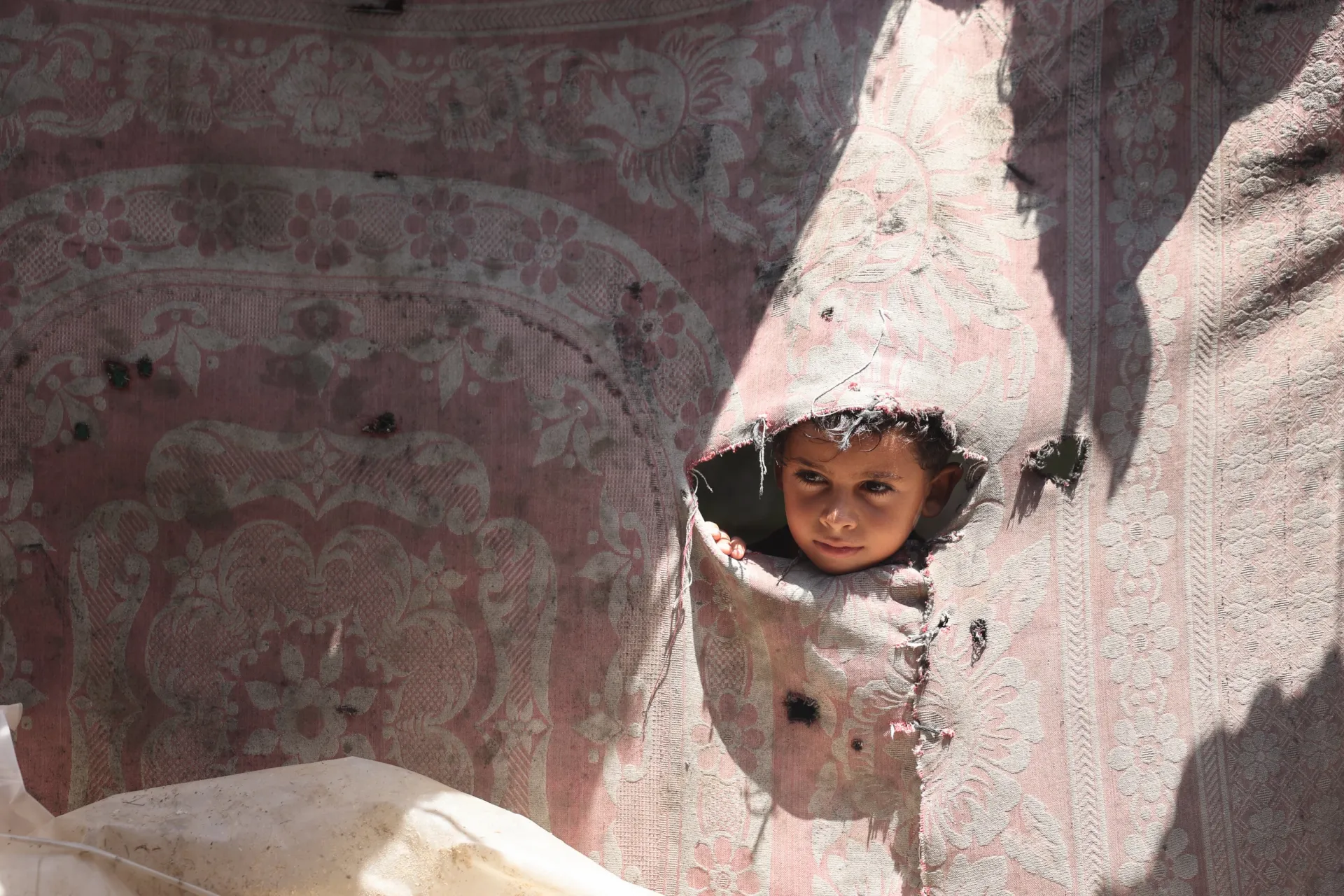 Jasser, a 7-year-old child from Gaza, looks out of one of the broken walls of a tent.