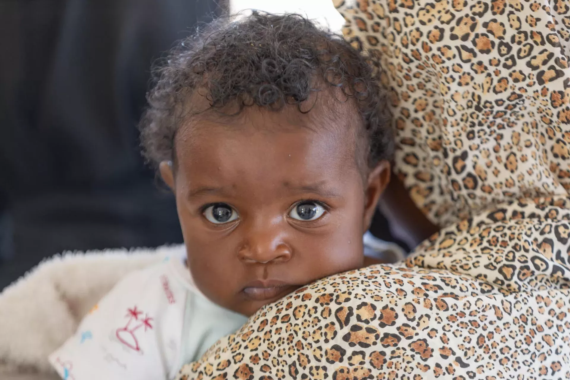 Sudan. A child looks over her mother's shoulder as she is held.