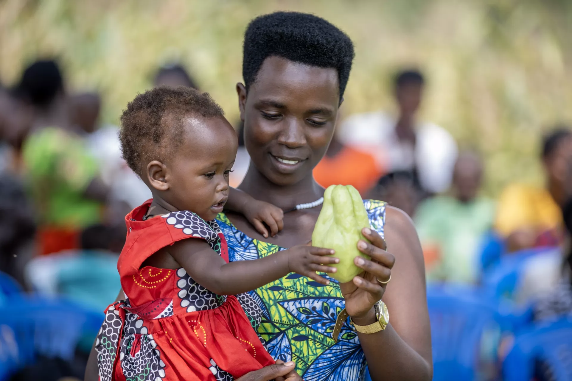 Musimenta Agnes holds a chayote squash fruit to her one-year-old daughter Atuhaire Provia at a community gathering showcasing the benefits of a community-led, UNICEF-supported initiative to combat malnutrition in western Uganda.