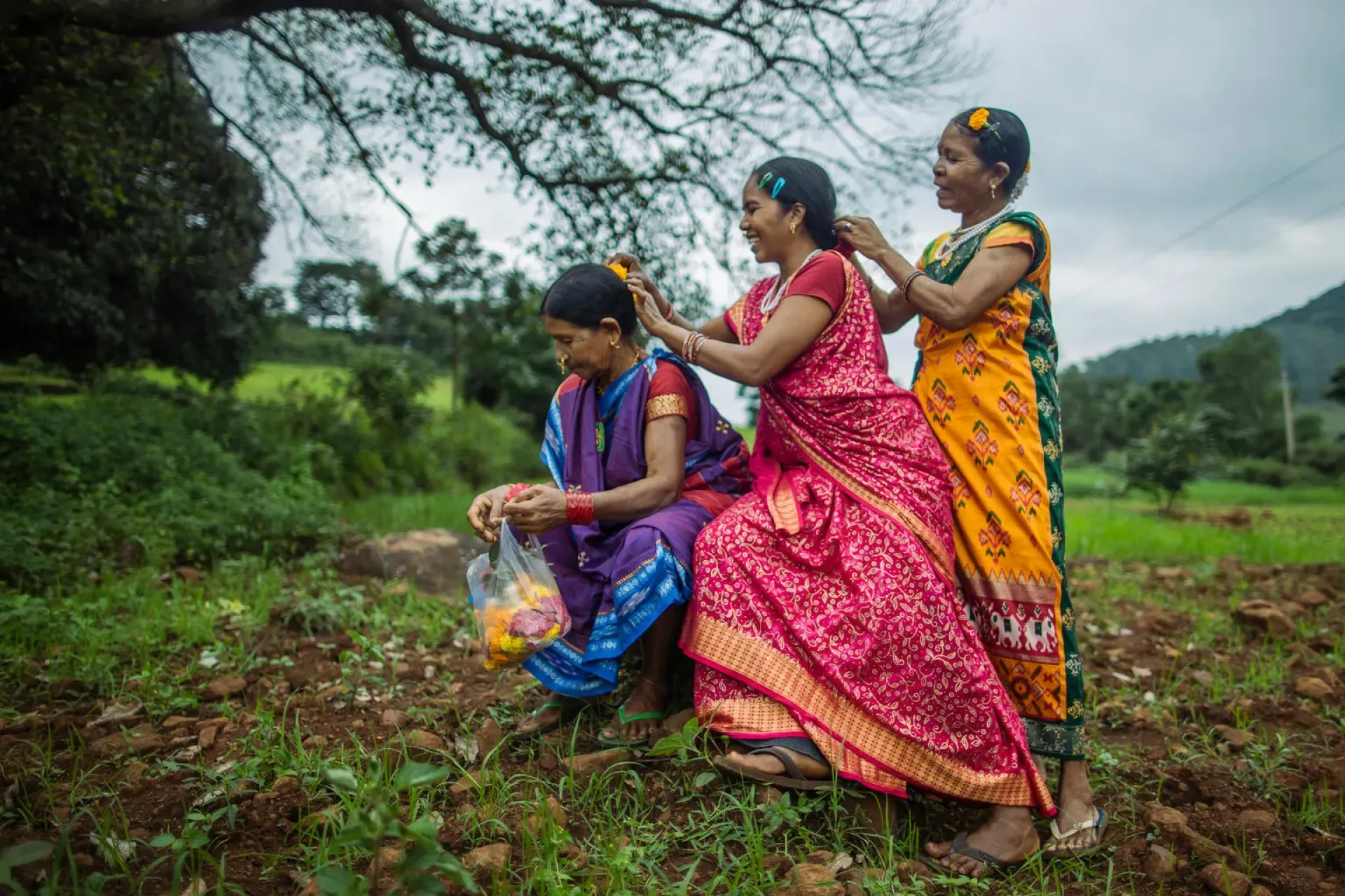 Three women in a field braiding each other's hair