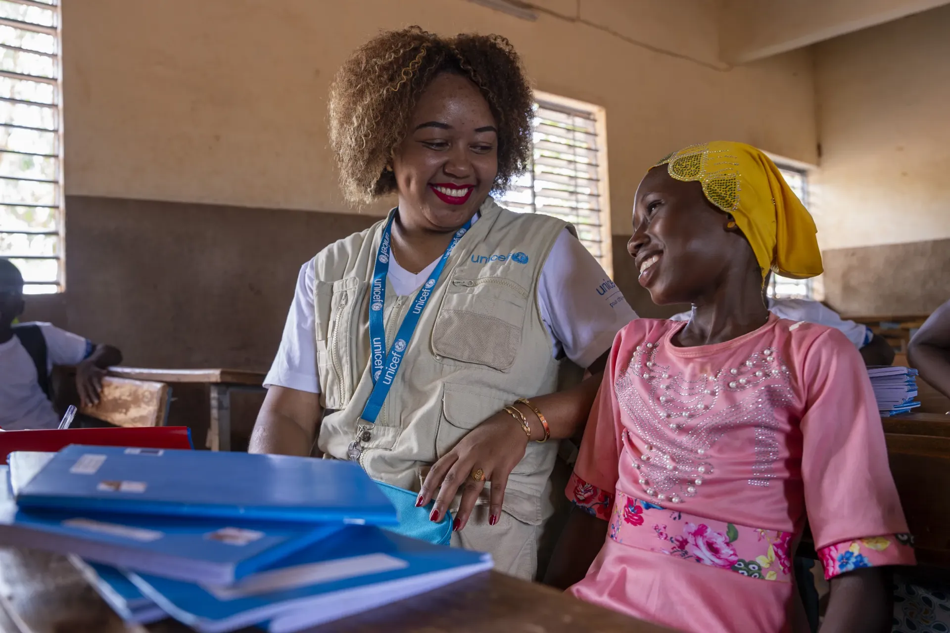 A UNICEF staff member sits with a smiling child in a classroom. 
